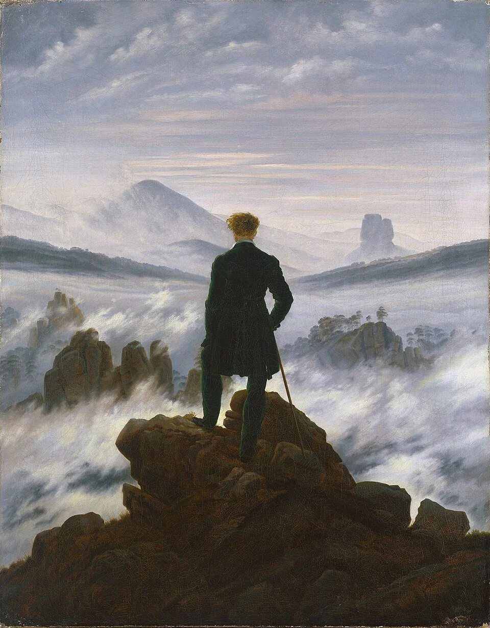 A man in a black coat and holding a cane standing on a rocky hilltop, overlooking a misty mountain landscape with clouds, distant mountains, and rock formations.