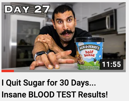 A man with a mustache sitting at a kitchen counter with an unamused expression, reaching towards a pint of Ben & Jerry's ice cream, in a modern kitchen setting.