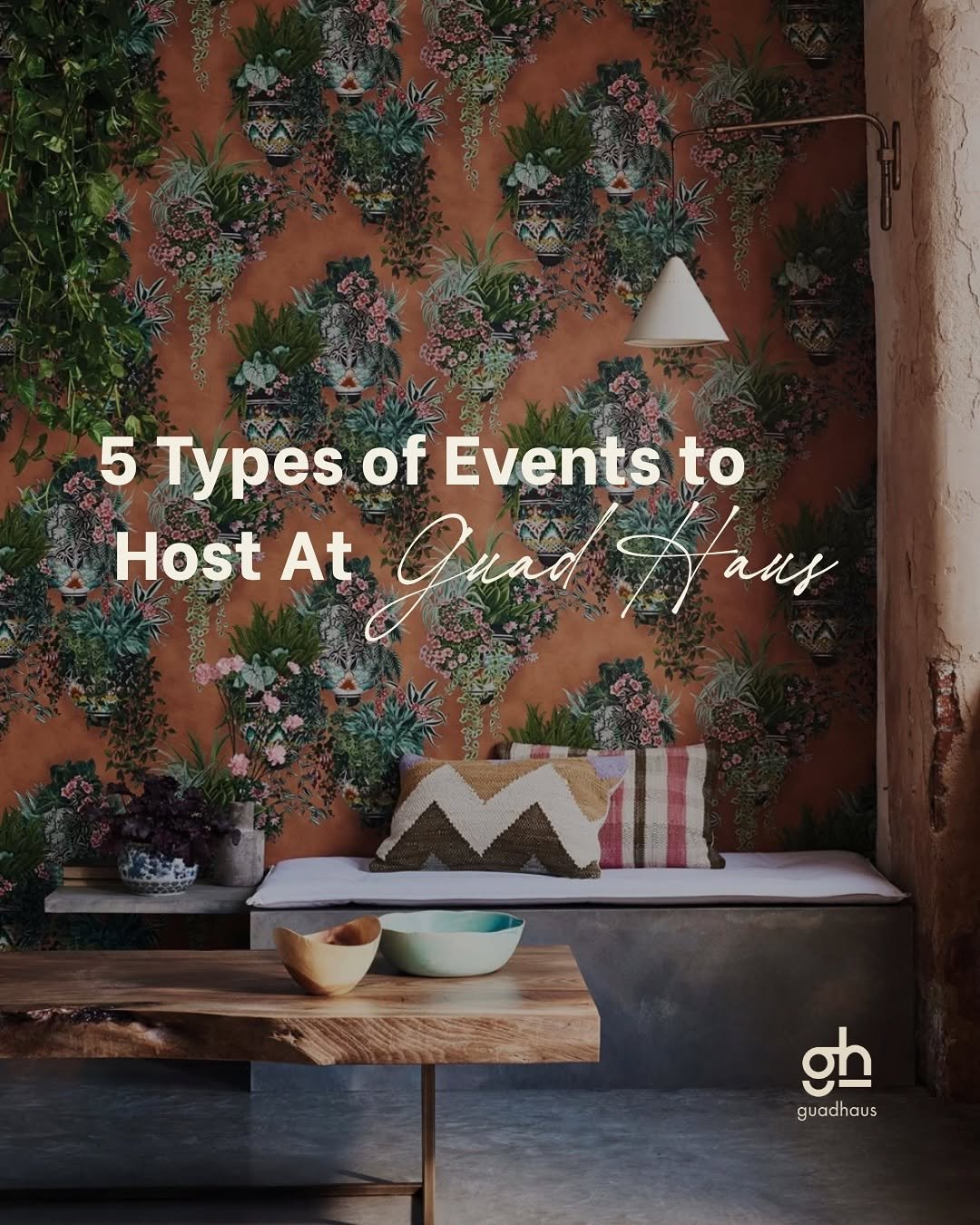 Interior of a rustic room with a floral wallpaper, a wooden table with bowls, a cushioned bench with patterned pillows, some potted plants, and a hanging lamp.