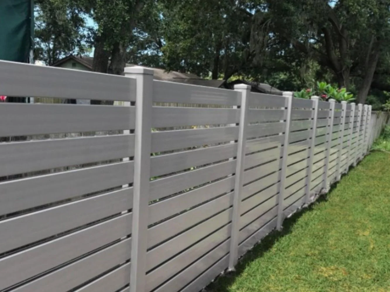 A white vinyl privacy fence extending along a grassy yard with trees and a house in the background.