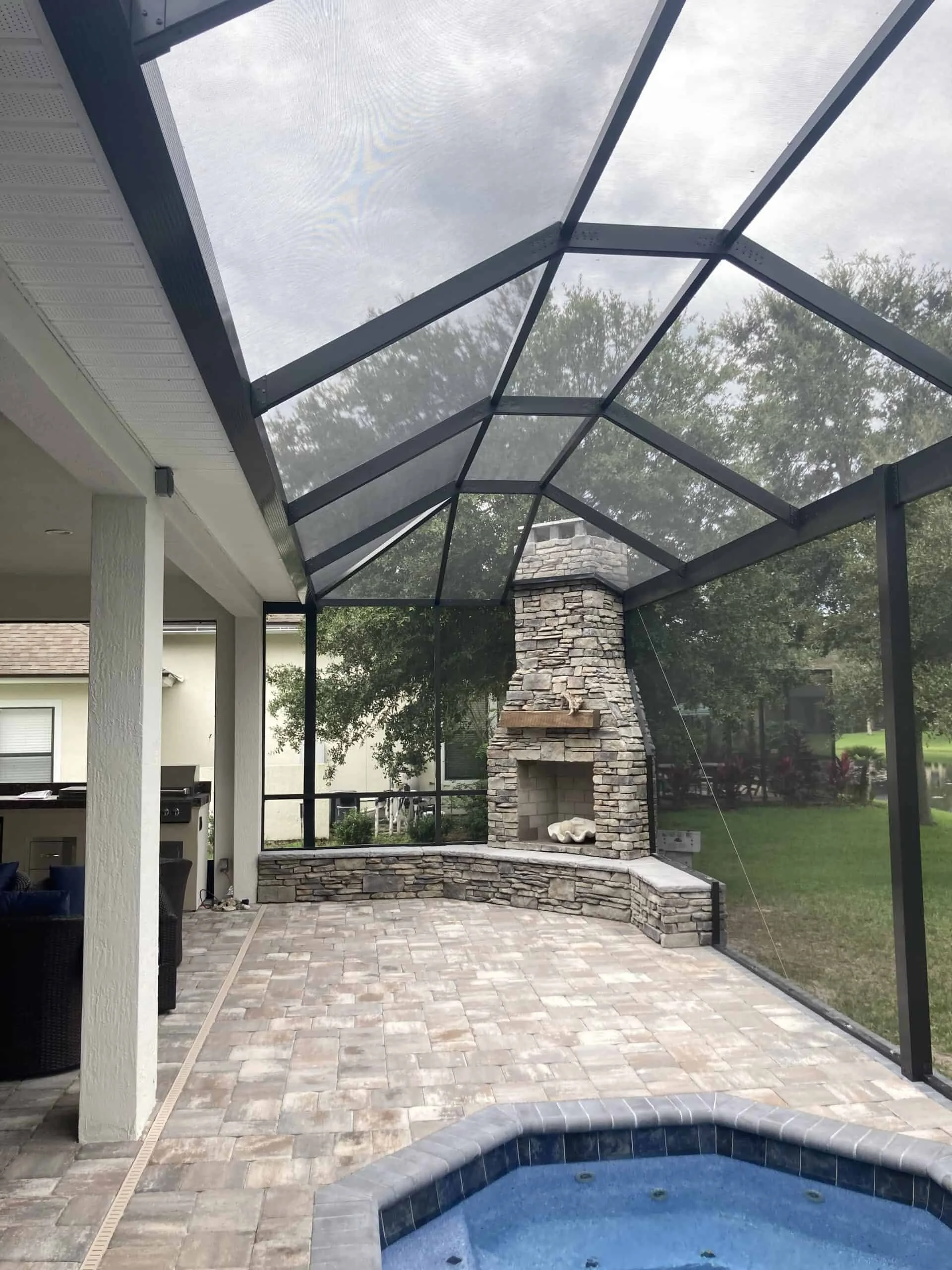 Enclosed outdoor patio area with stone fireplace, brick paver flooring, pool, and a screened glass roof.
