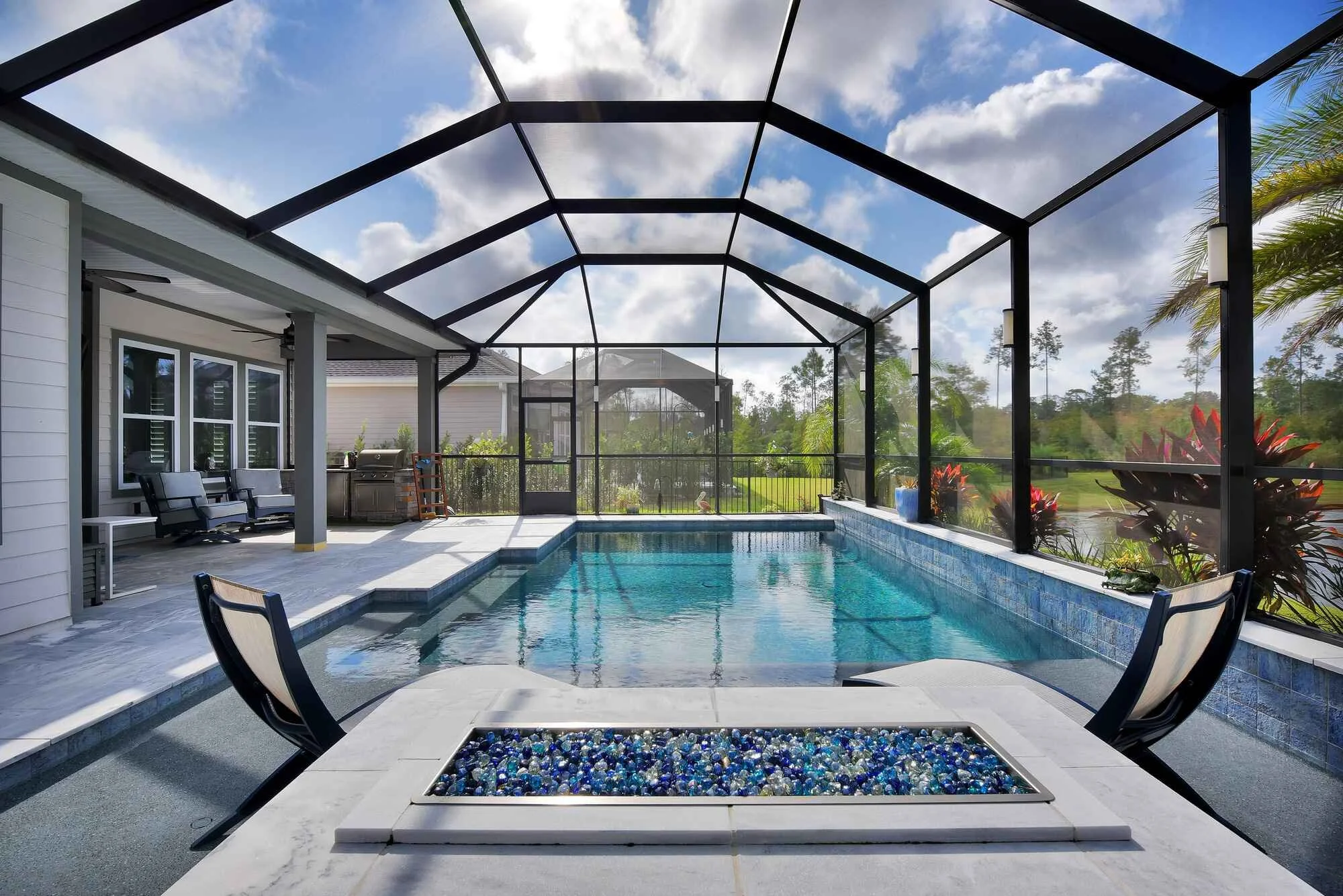 Covered backyard swimming pool with outdoor seating area and trees in the background under a partly cloudy sky.