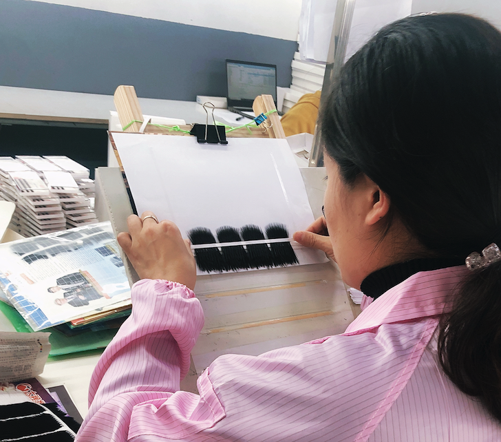 Woman inspecting cosmetic eyelash extensions in a beauty salon or workshop.
