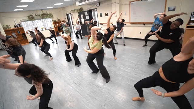 A group of people dancing or practicing in a dance studio with mirrors and wooden shelves.