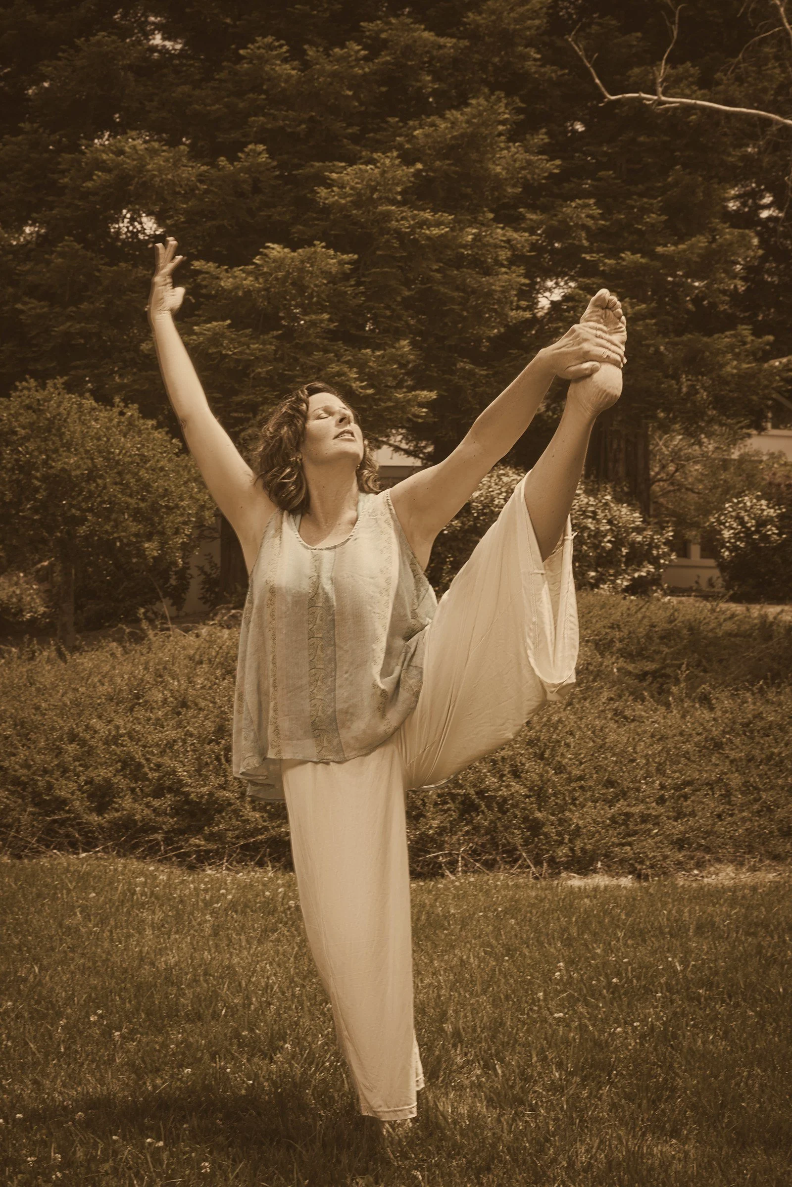Jessica Batha dancing outdoors, one arm and one leg reaching toward the sun