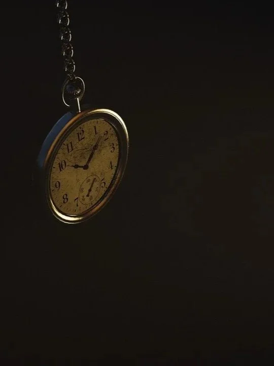 A vintage pocket watch hanging from a chain, showing the time as 11:09, against a dark background.