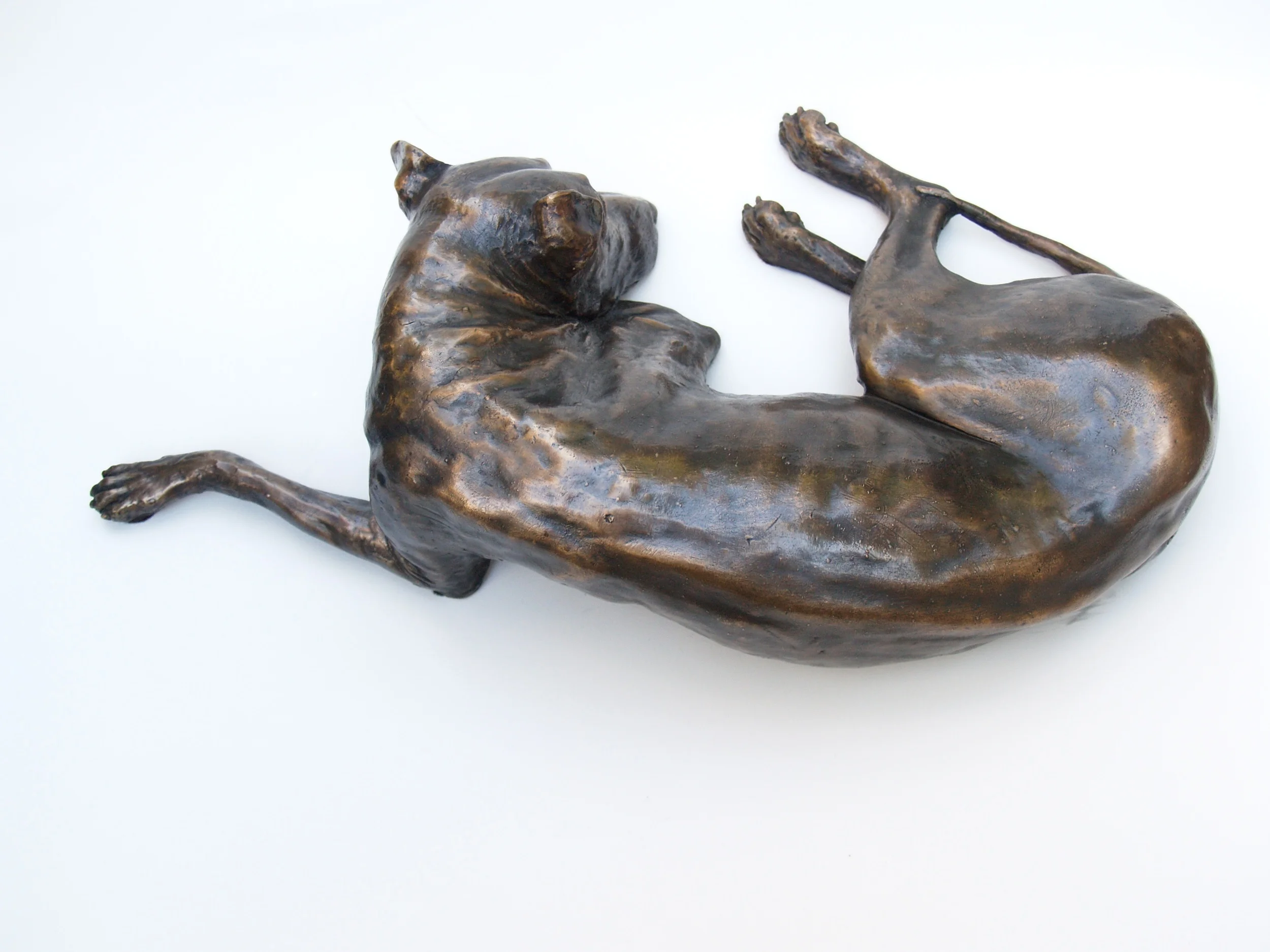 Bronze sculpture of a reclining dog on a white background.