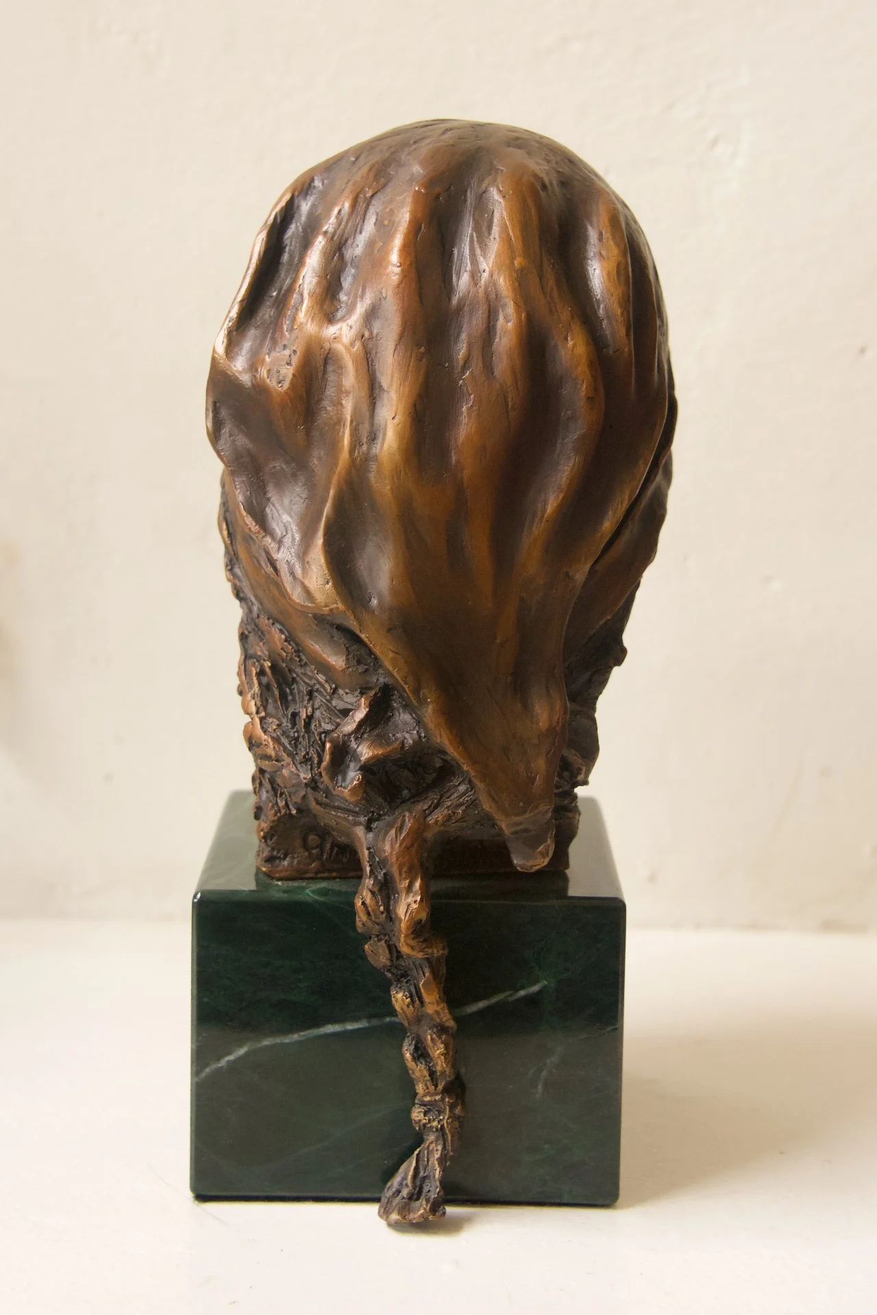 A bronze sculpture of a headless figure, with a flowing, abstract form, mounted on a dark green marble base.