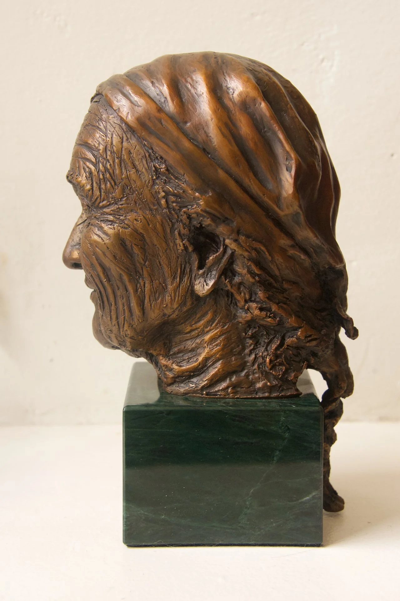 Bronze sculpture of a man's profile with long hair and a beard on a green rectangular base.