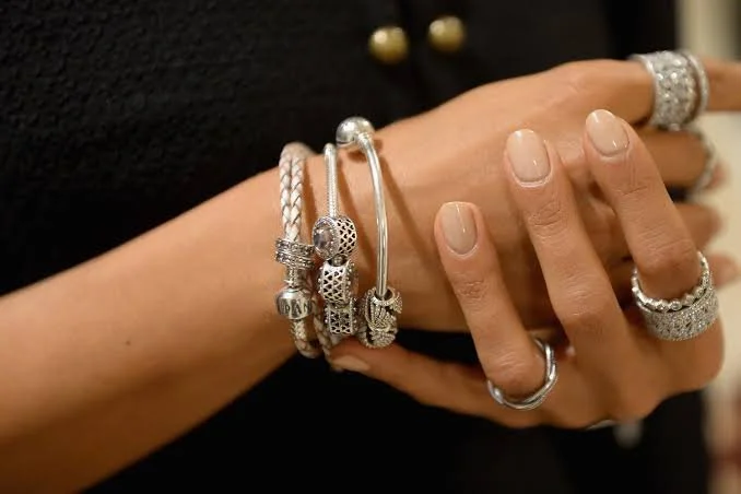 Close-up of a woman's hand and wrist adorned with multiple silver rings and bracelets, with a black top with gold buttons in the background.