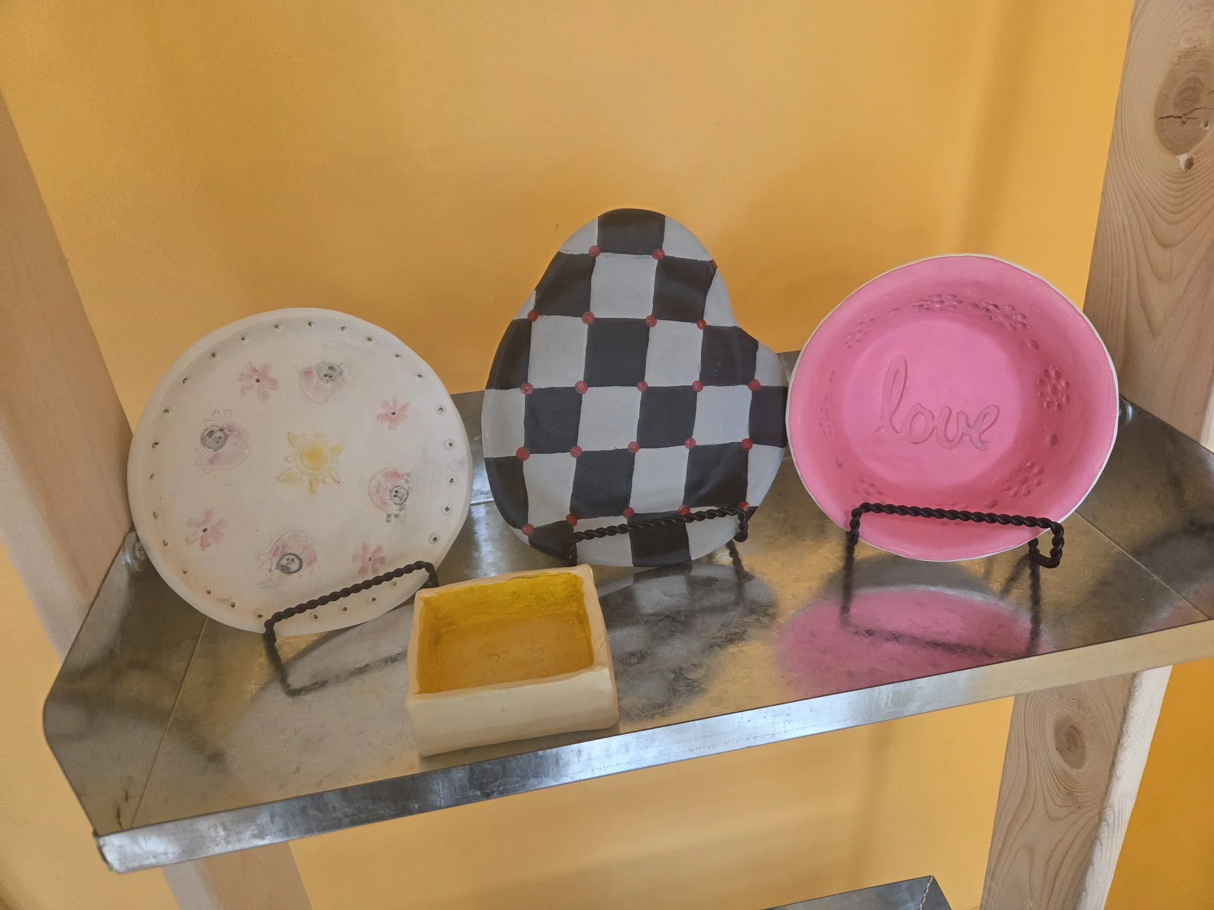 Decorative trinket dishes in various styles and color designs. The dishes are on black wire stands against a yellow wall.