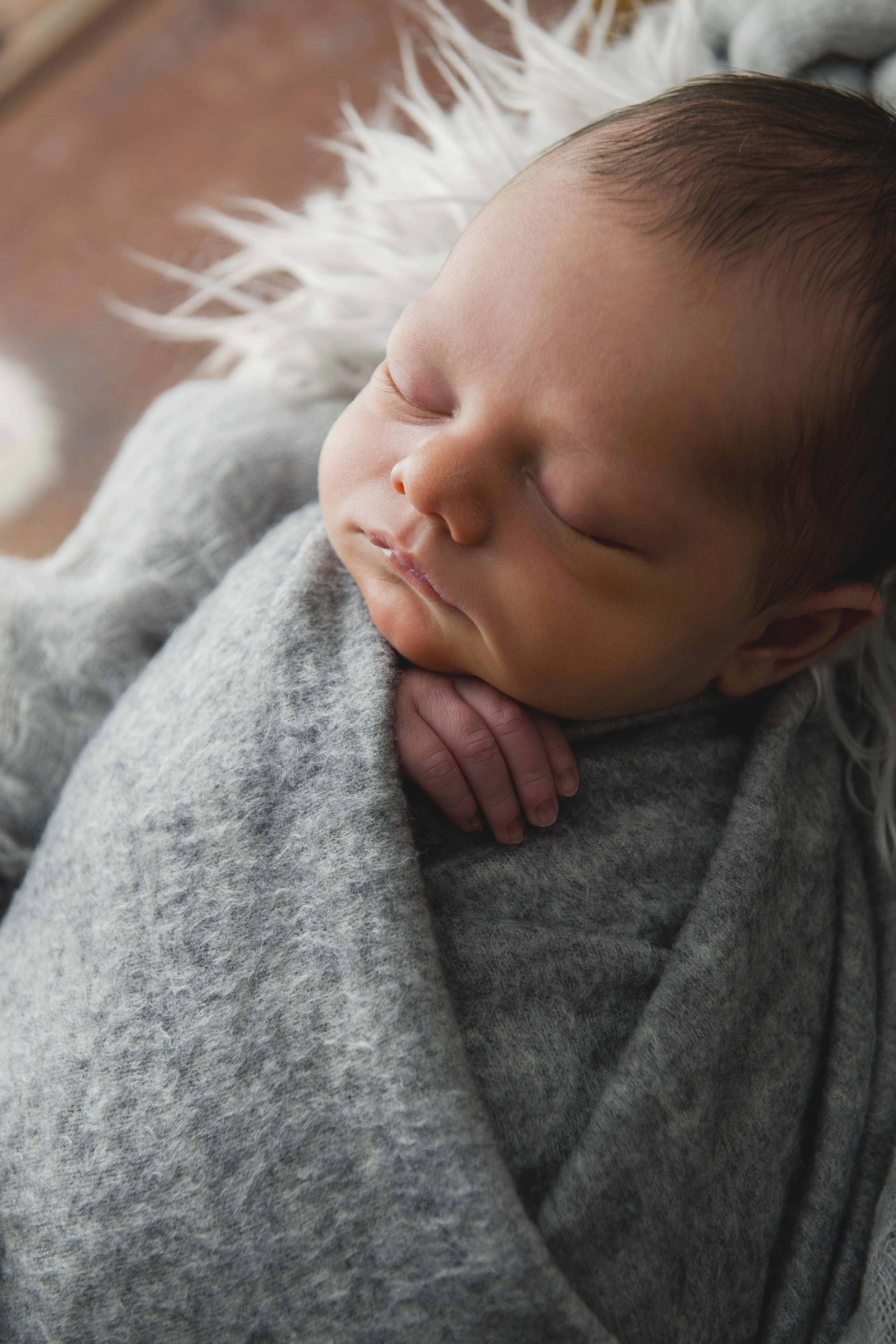 A sleeping baby with closed eyes, resting peacefully against an adult's shoulder, wrapped in a soft gray hoodie.