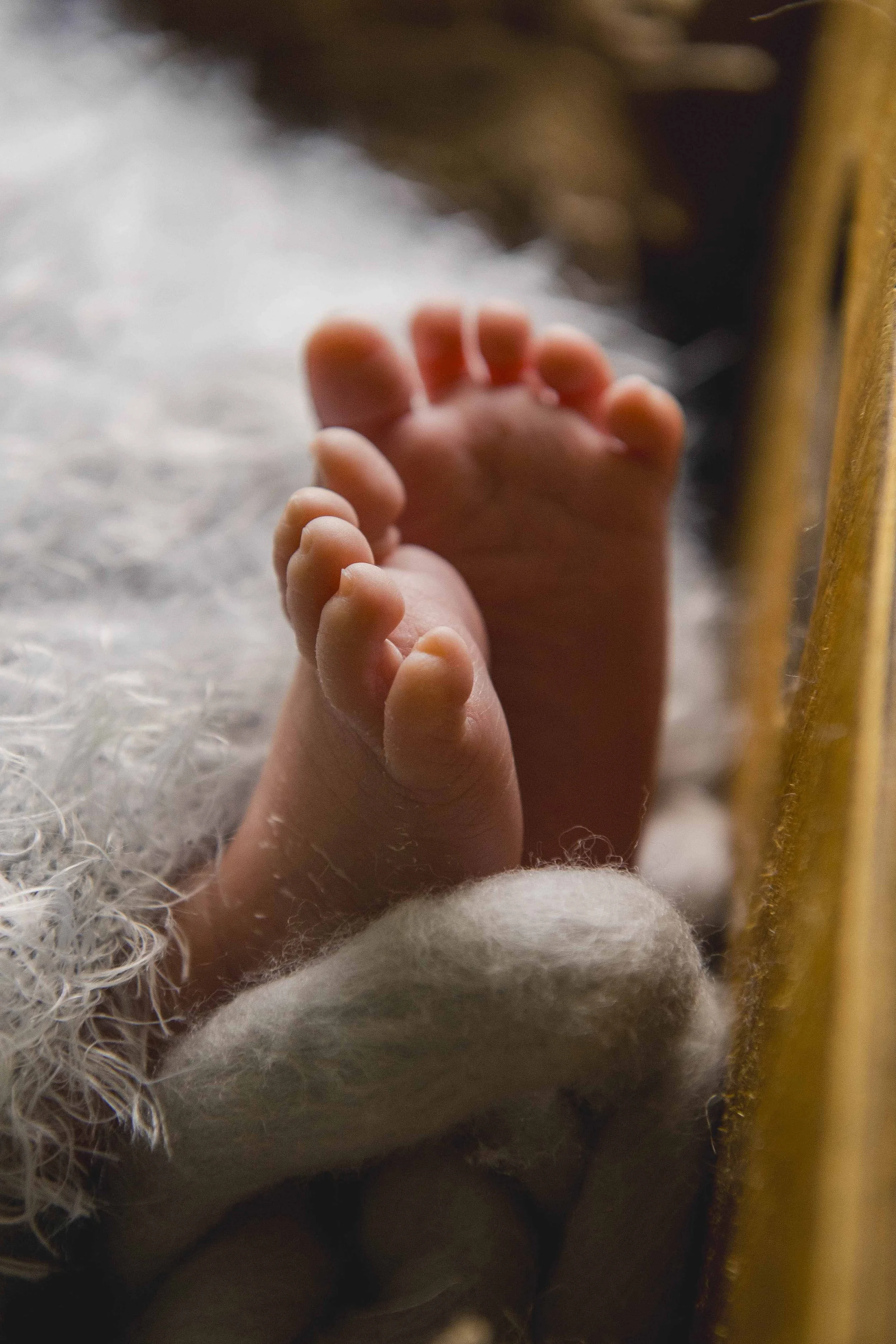 Close-up of a newborn baby's toes, with soft background and a yellow wooden surface on the side.