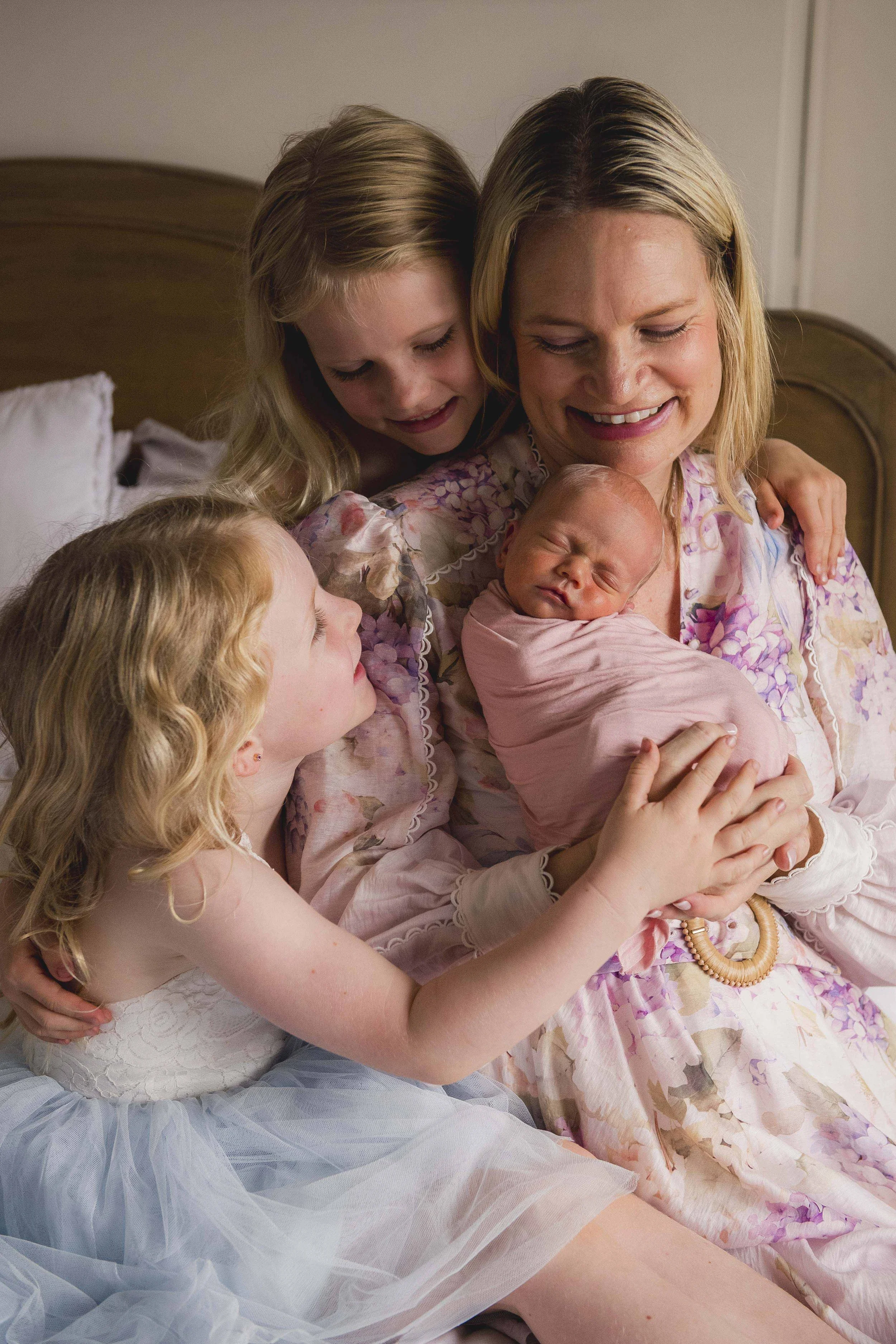 A woman holding a newborn baby, surrounded by her young girls in a cozy room.
