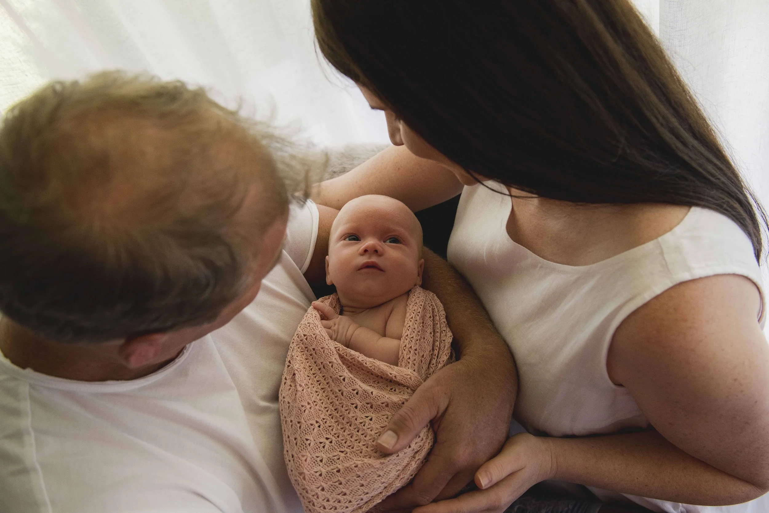 A baby girl lies in a woman's arms, looking up at her. The scene is intimate and warm, set indoors with neutral background.
