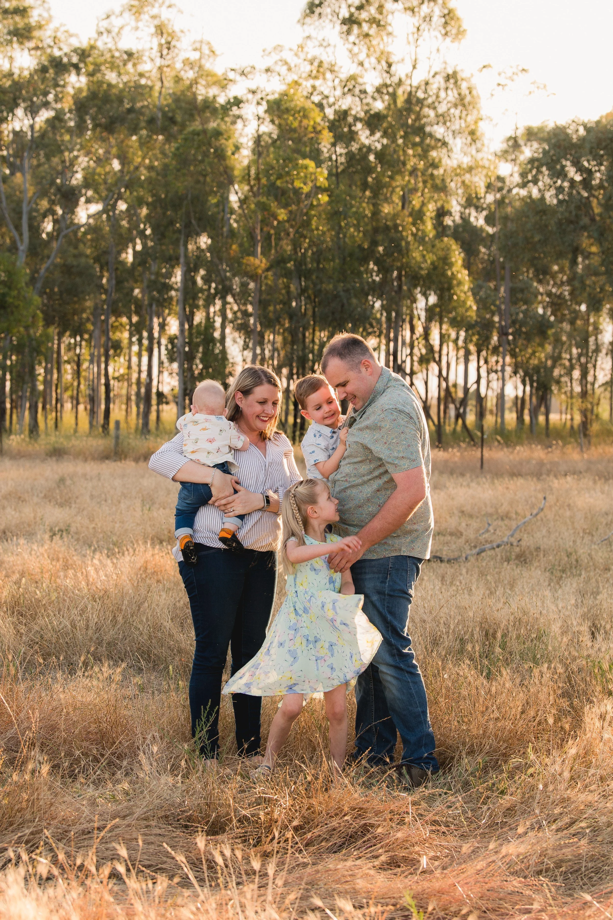 Family of six enjoying a walk in a field during sunset, with tall grass and trees in the background.