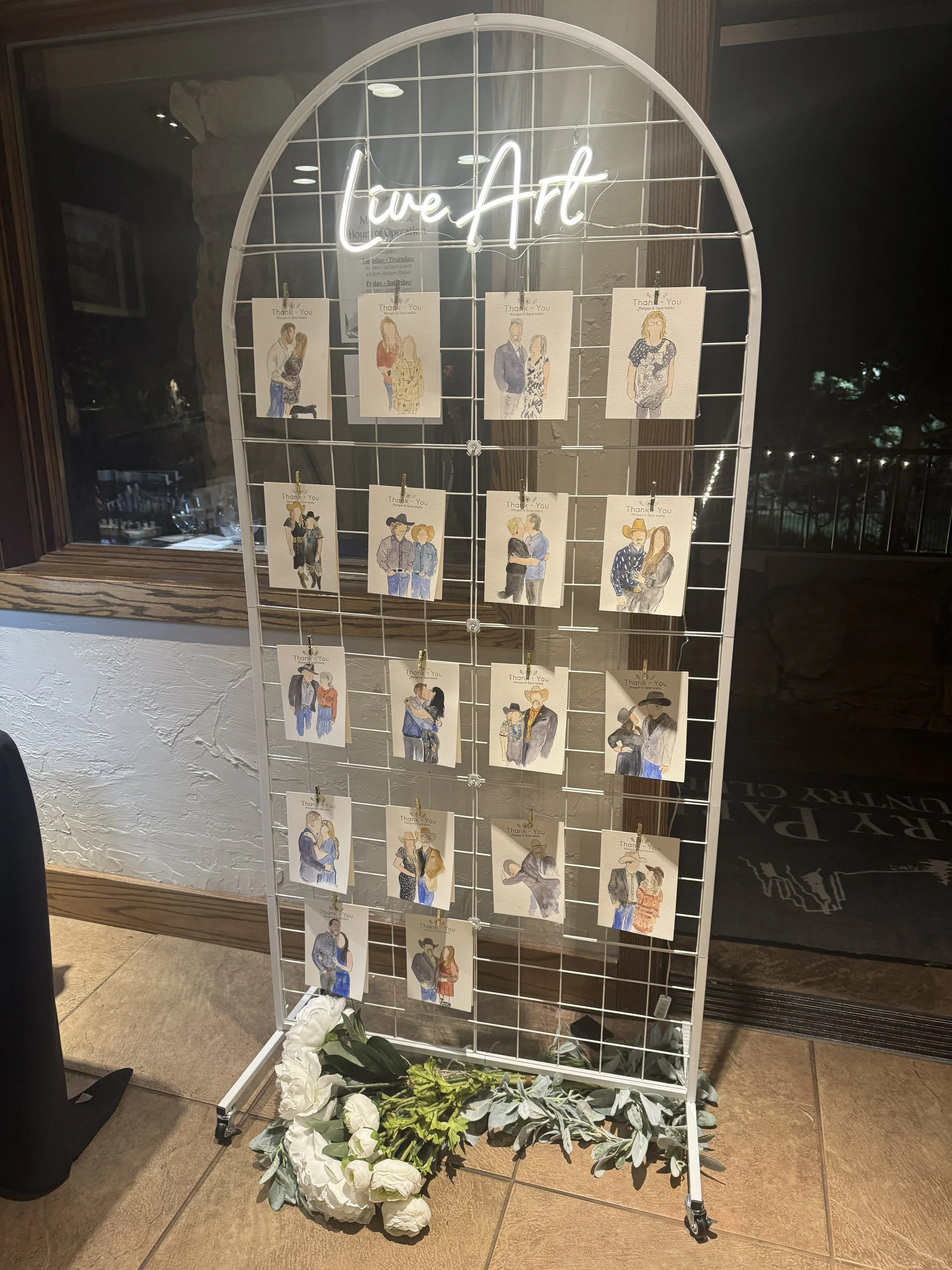 Display stand with watercolor illustrations of couples, titled 'Live Art', decorated with white flowers at the base.