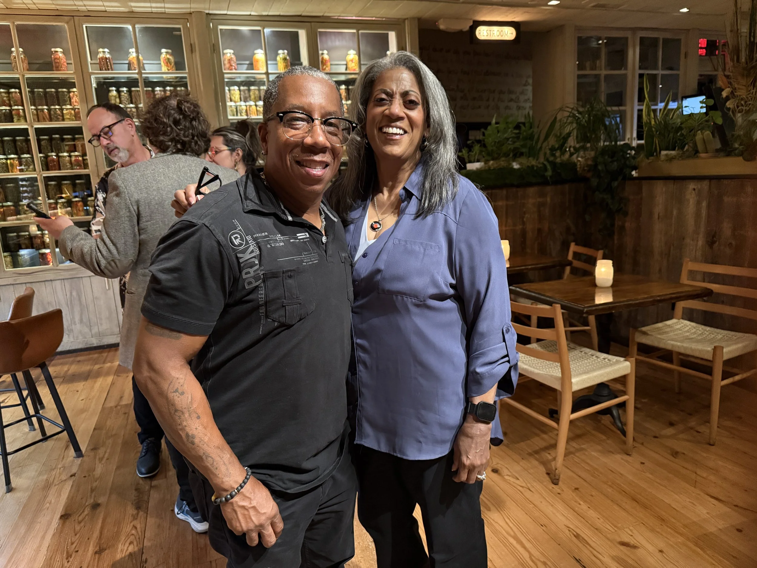 Tim Hutson on the left with Anita Guris on the Right. Smiling for the camera. Happy to be at SOUTH Jazz Club with Paul Guris in the background talking to a friend's son.