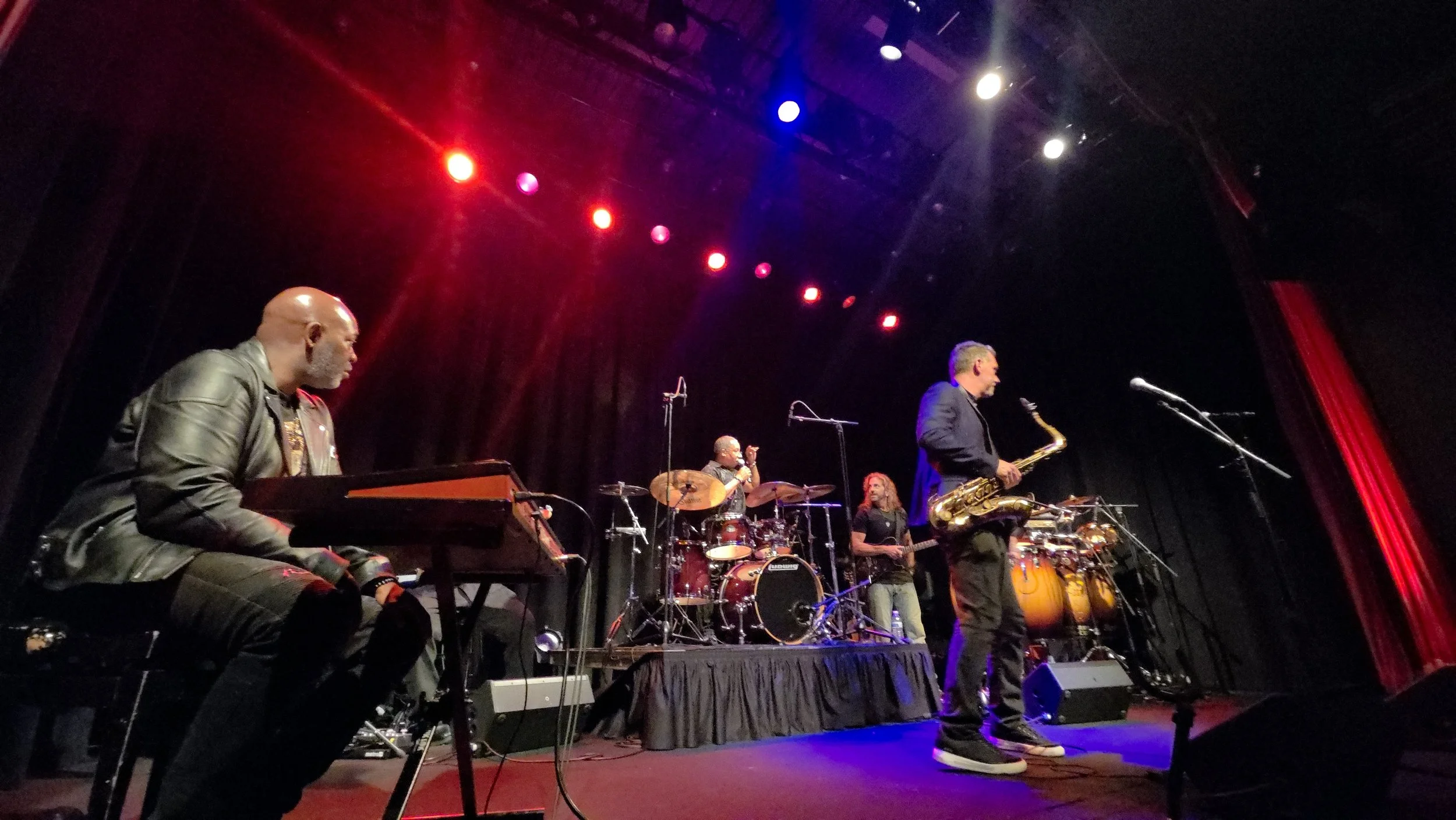 Tim Hutson and the Carl Cox Sax Syndicate -  live band performing on stage at Sellersville Theater with instruments including keyboard, drums, and saxophone under colorful stage lighting.