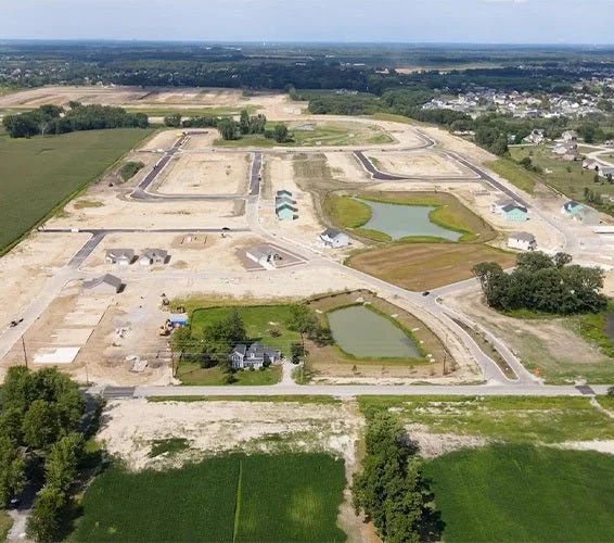 Aerial view of a residential construction site with newly built roads, some houses, and active pond construction in a semi-rural area.
