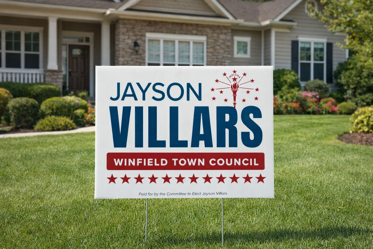 Political campaign yard sign for Jayson Villars supporting Winfield Town Council, featuring a red, white, and blue color scheme, with a torch and fireworks icon at the top, placed on a well-manicured lawn in front of a house.