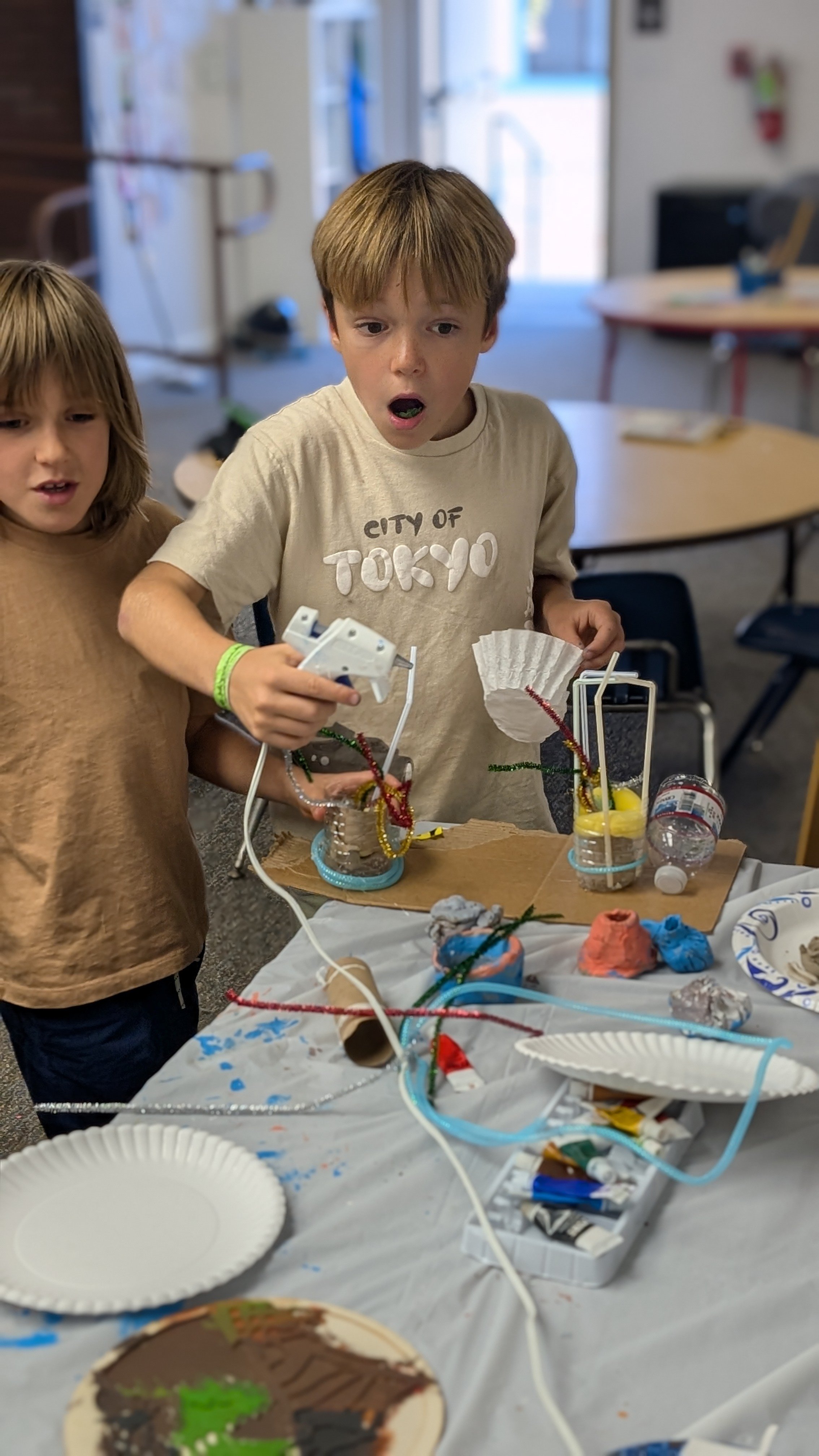 Children engaging in a science or art project at a classroom table, with various craft supplies, paper plates, and colorful materials scattered across the table. they are exited to participate in hands-on learning. 