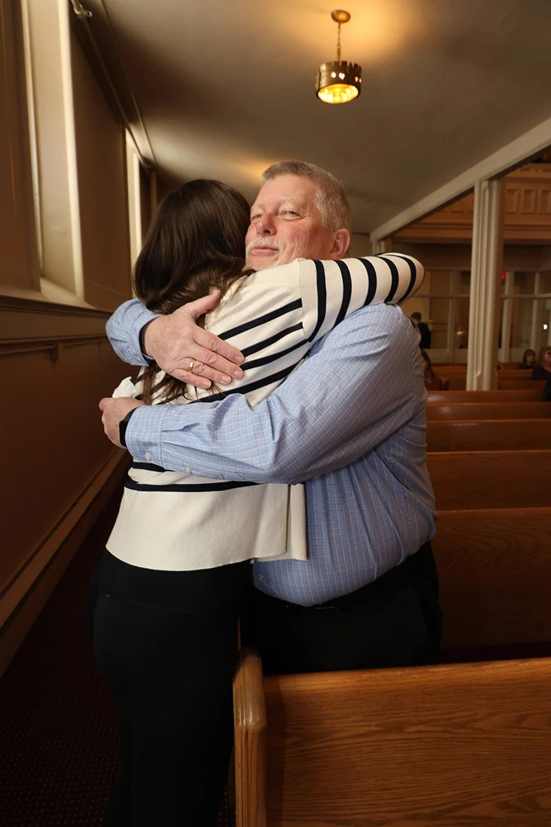A man and a woman hugging each other warmly inside a church or similar setting.