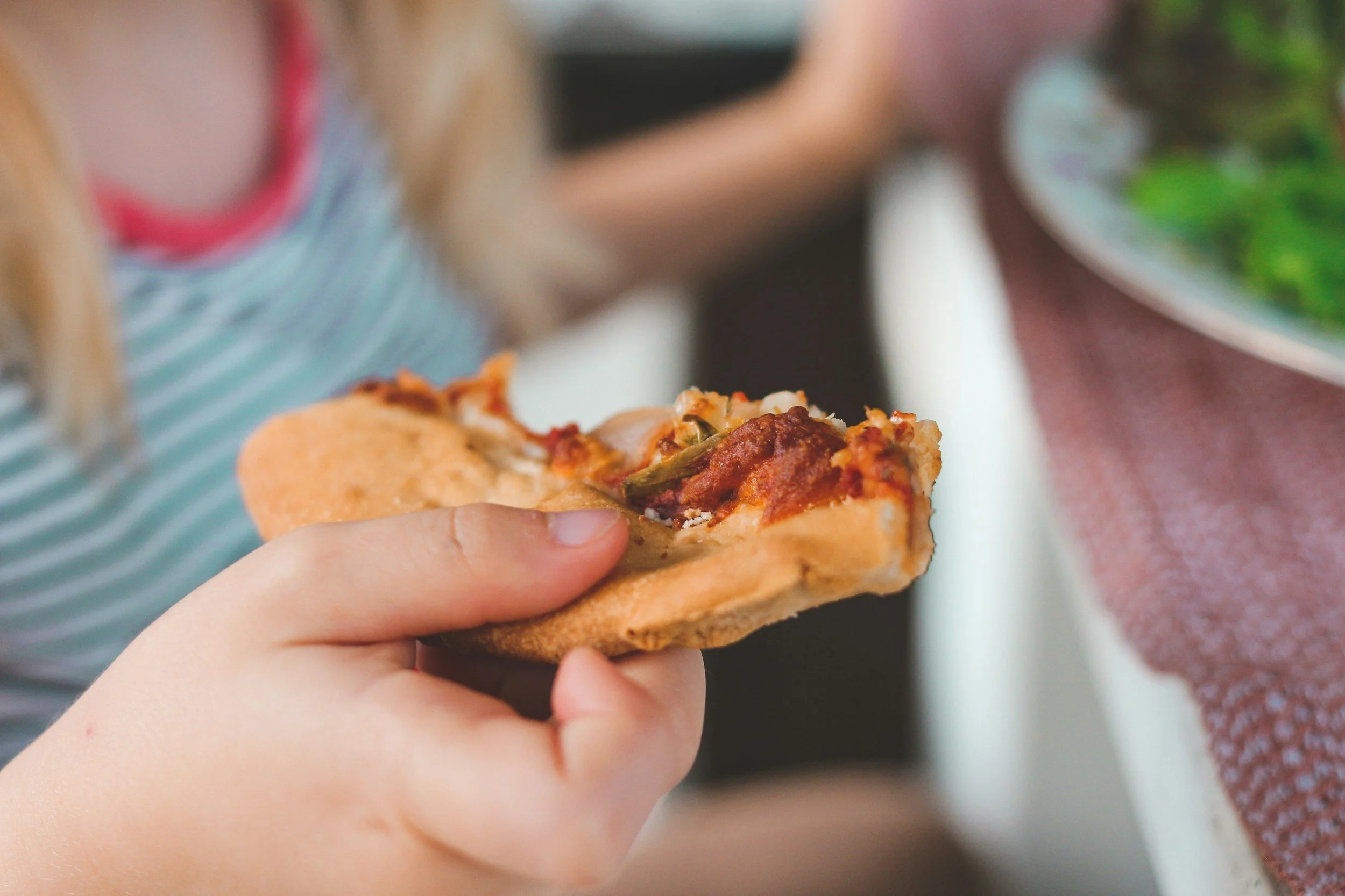 A person holding a slice of pizza with meat and vegetables
