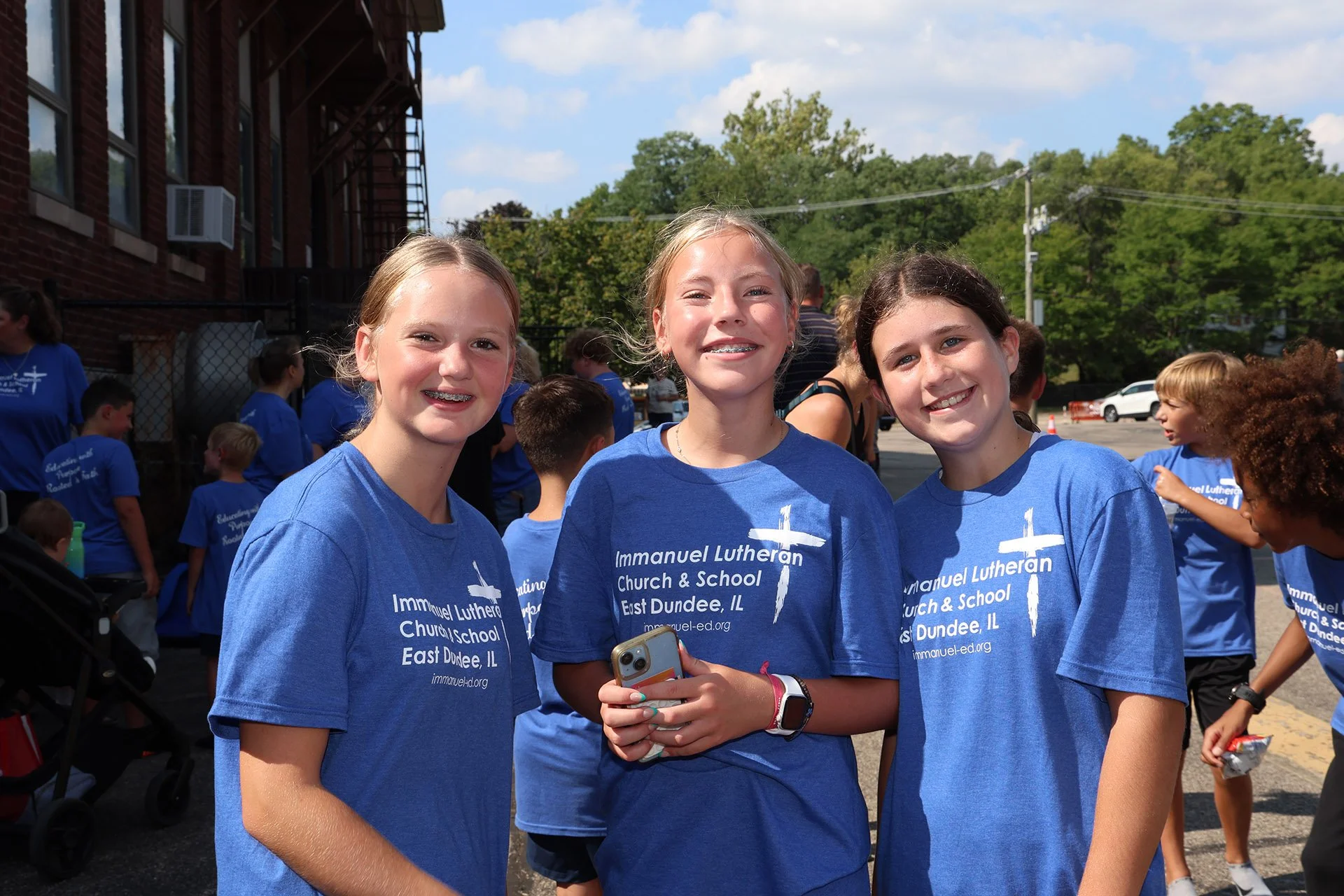 Group of young girls wearing blue T-shirts from Immanuel Lutheran Church & School, East Dundee, Illinois, smiling at an outdoor event.