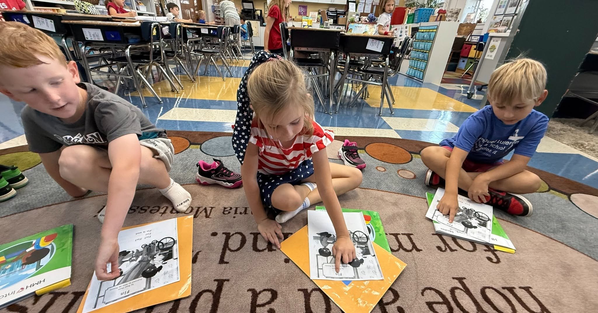 Three young children sitting on a rug in a classroom, reading books.
