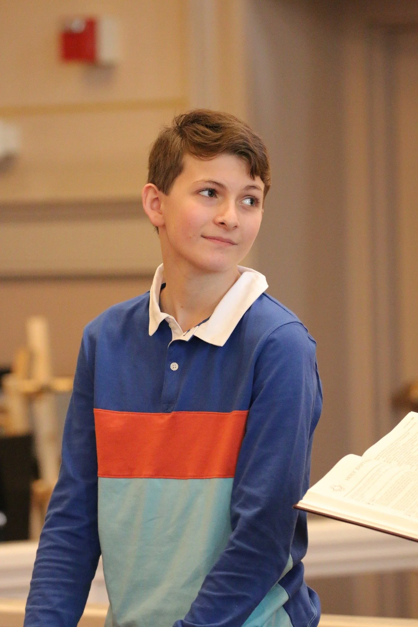 A young boy with short brown hair, wearing a multicolored polo standing in Immanuel Lutheran Church.