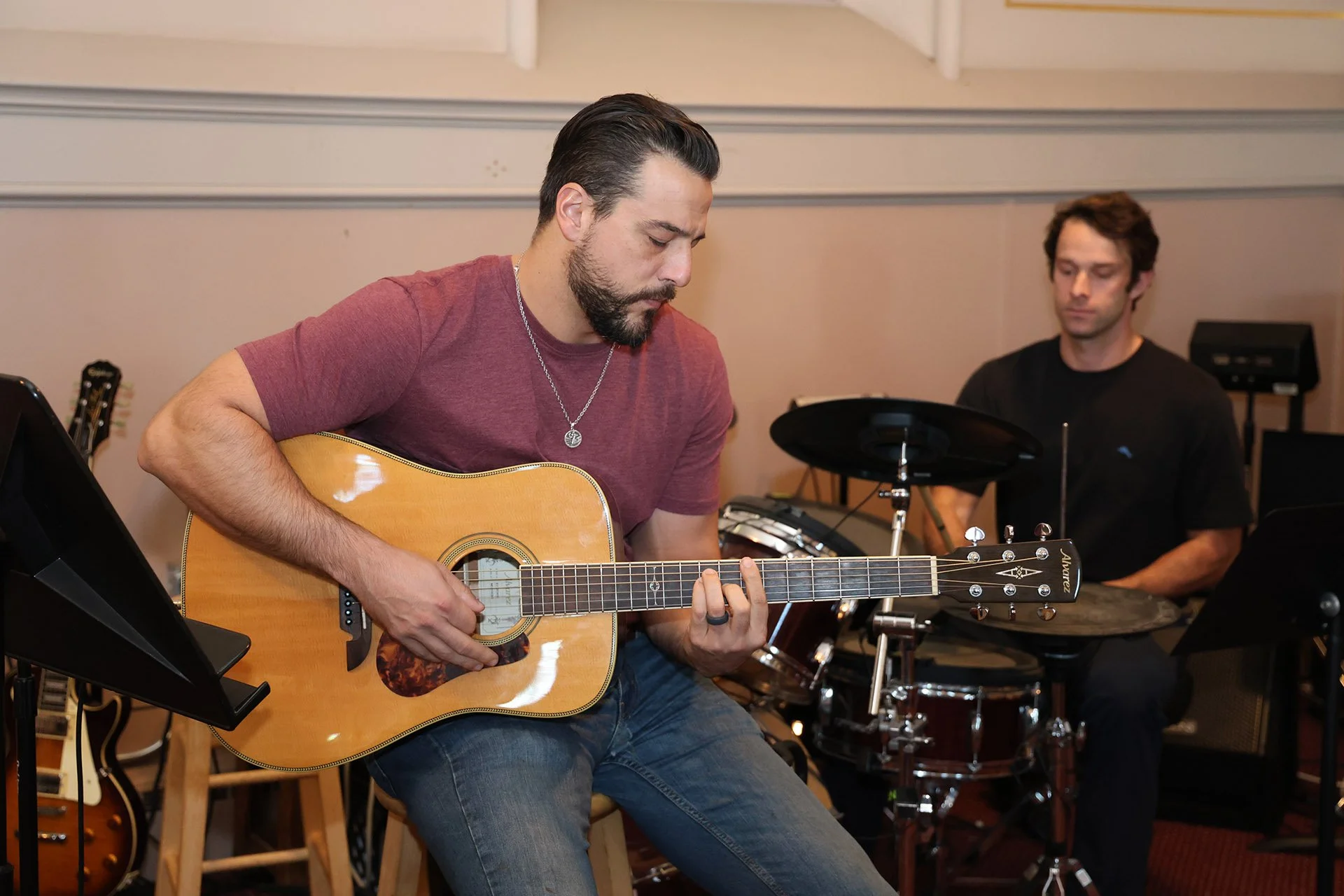 A man with dark hair and a beard playing an acoustic guitar for contemporary service.