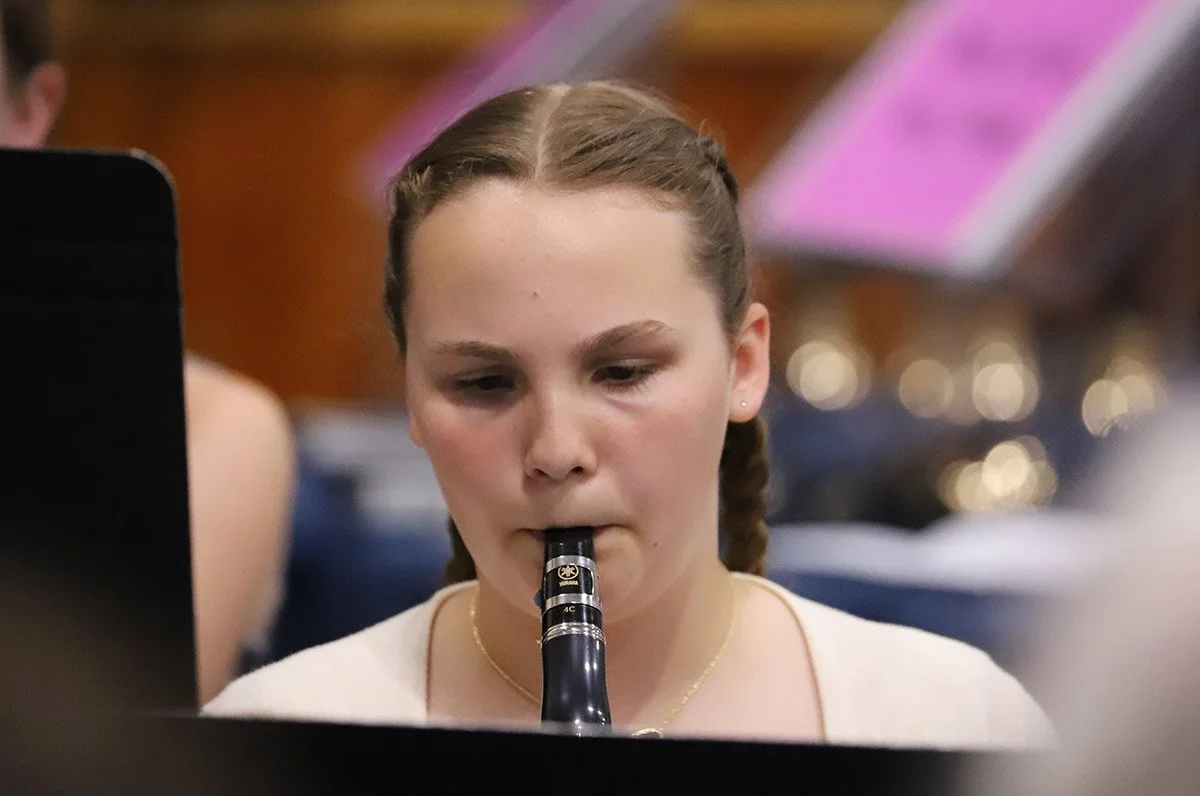 A young woman with braided hair playing a clarinet in a performance or practice setting.