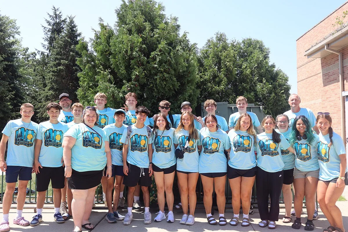 Group of teenagers and adults wearing matching light blue T-shirts.