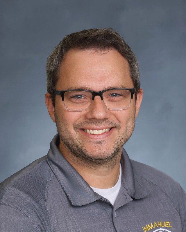 A smiling man with glasses and short brown hair wearing a gray collared shirt.
