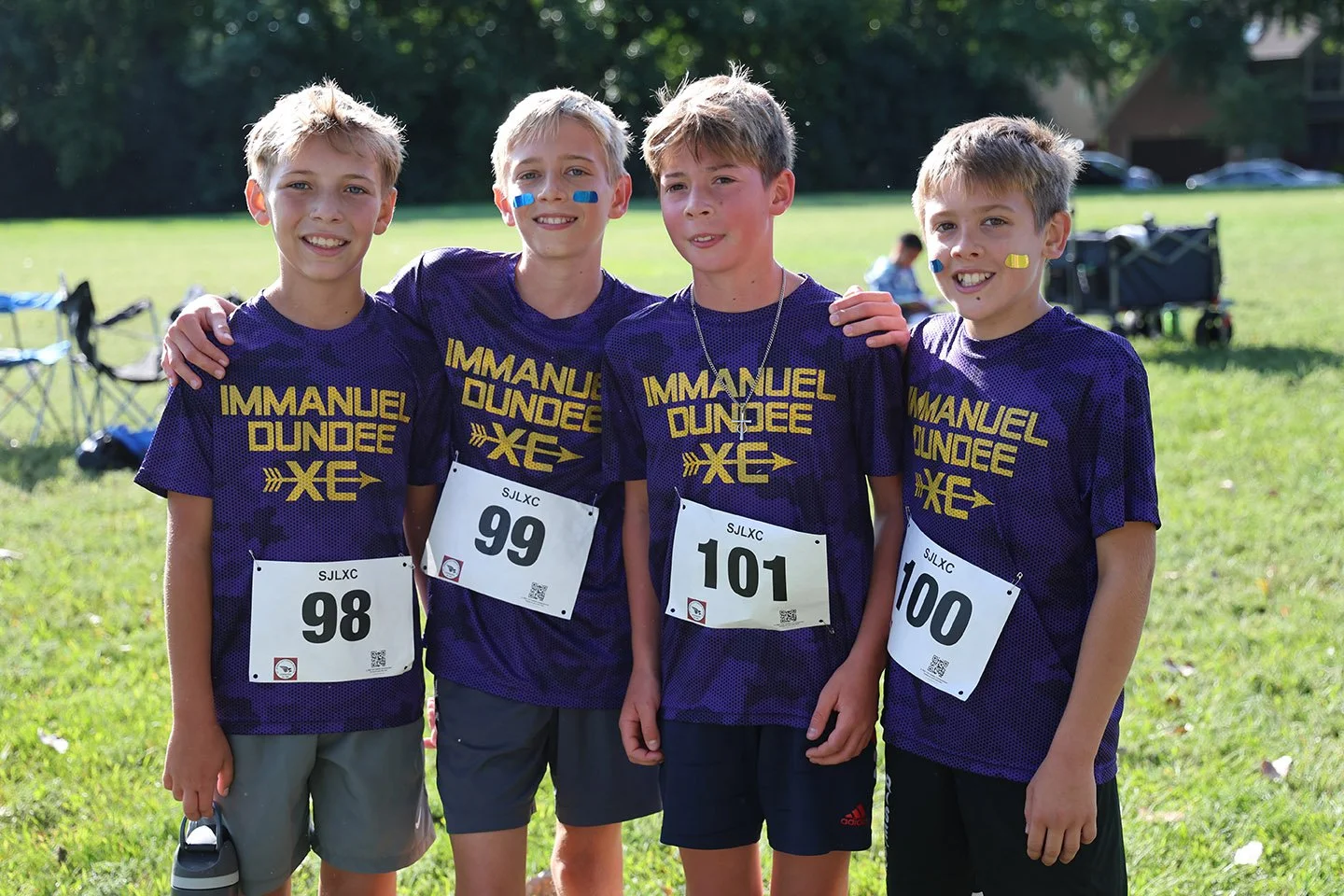 Four young boys wearing matching purple sports jerseys with 'Immanuel Dundee XC' printed on them.