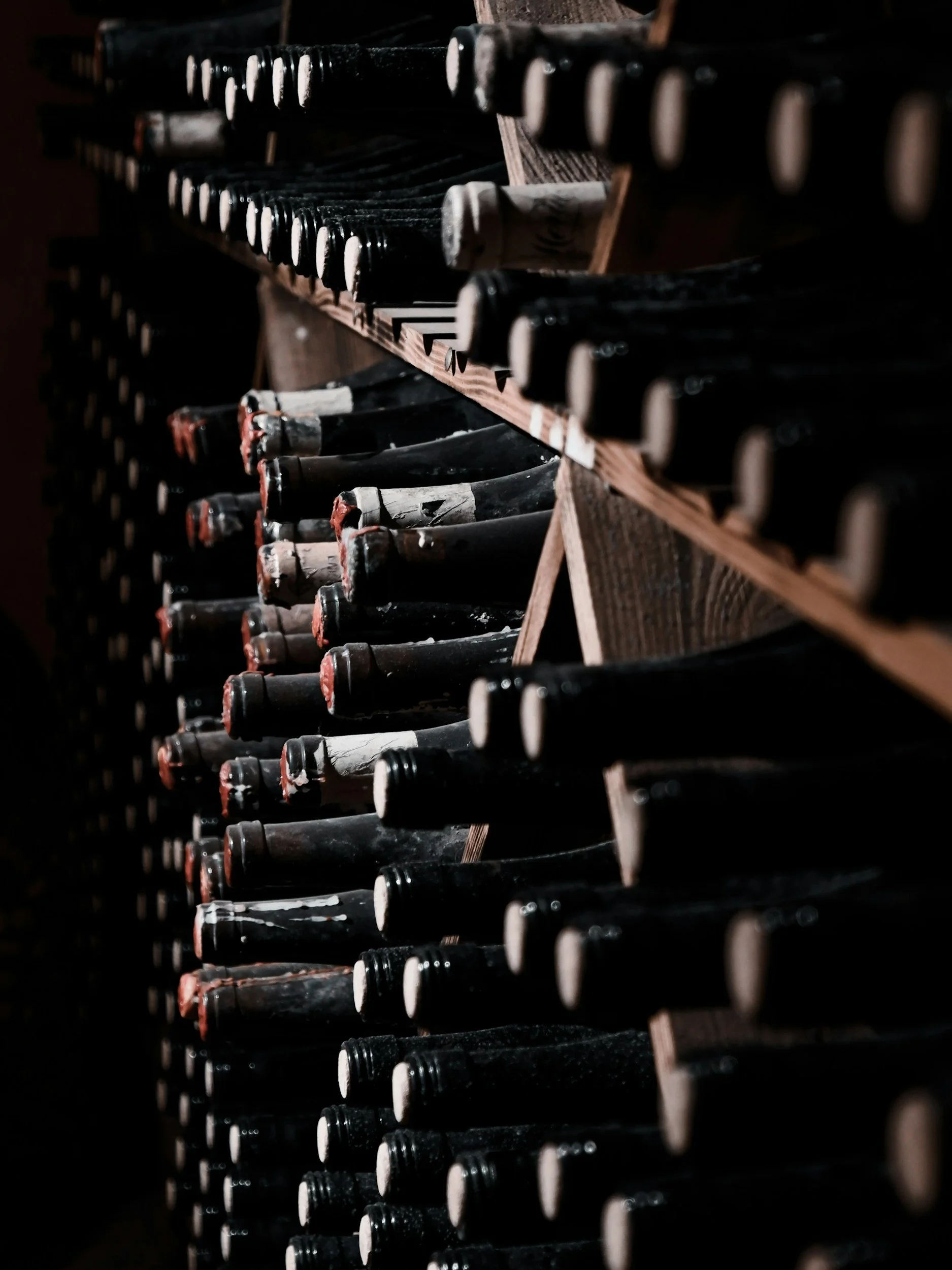 Rows of wine bottles stored on wooden racks in a dark cellar.