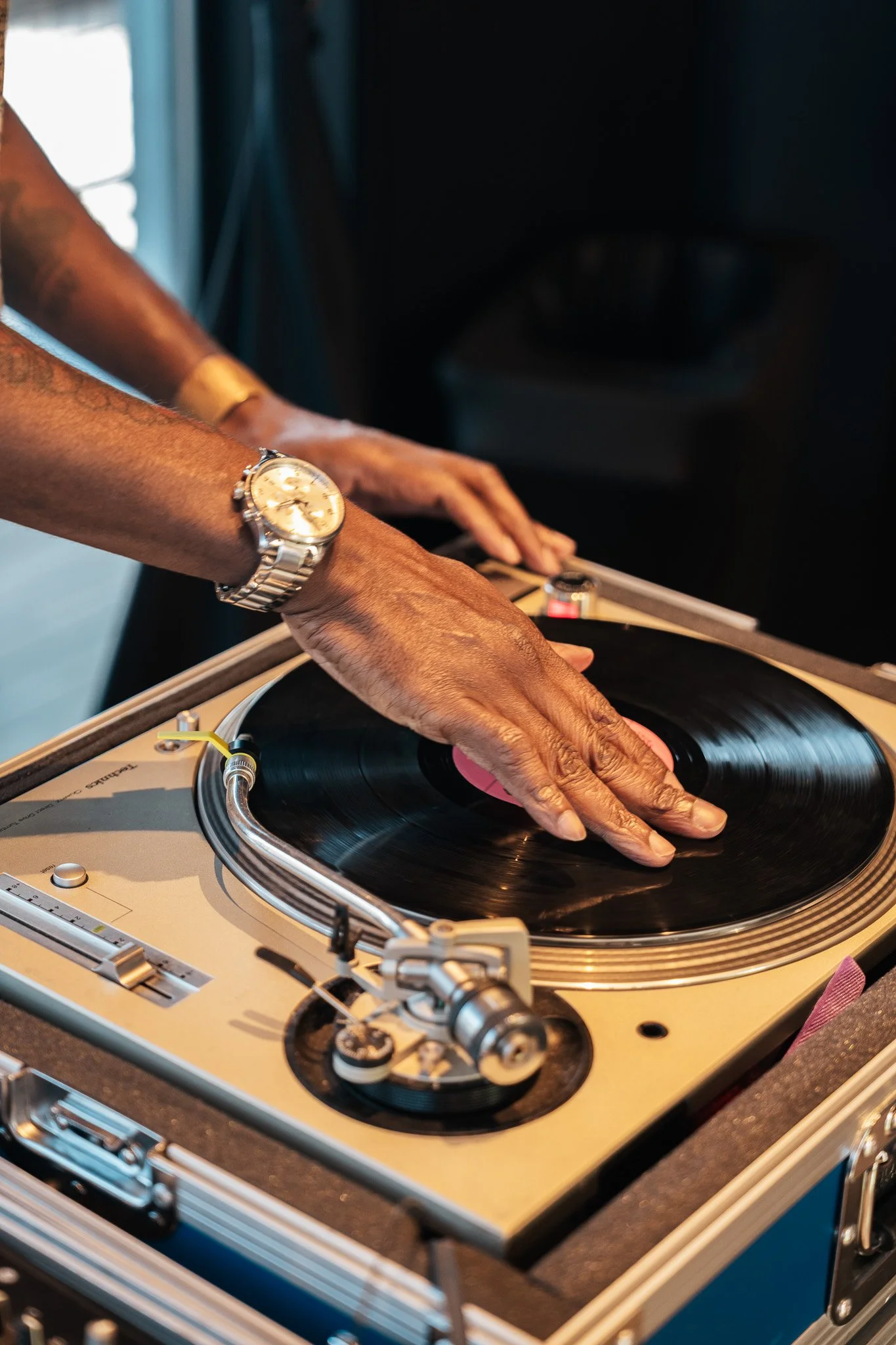 Close-up of a person djing on a turntable, wearing a watch and placing a vinyl record on the record player.