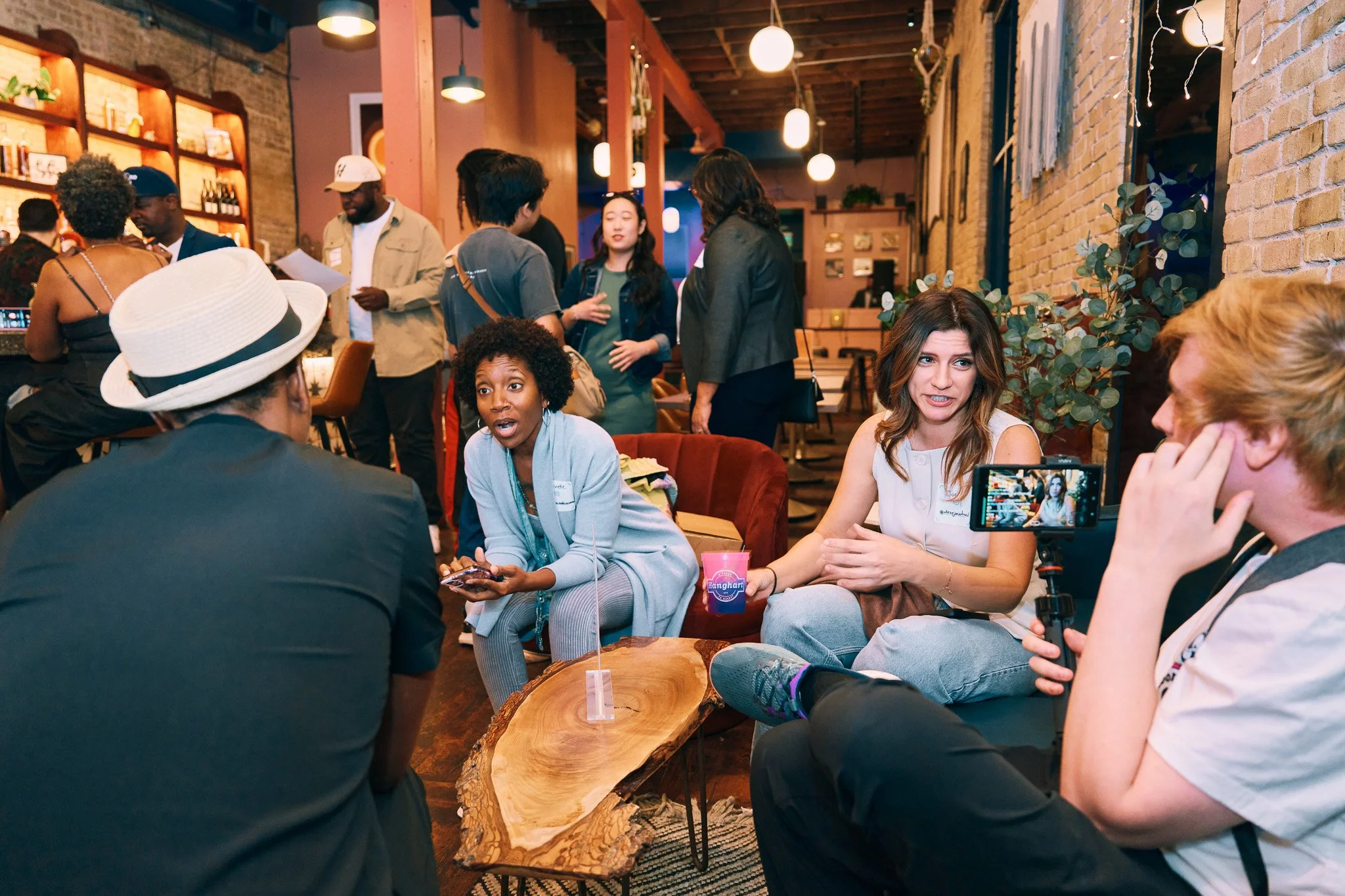 A group of men and women engaged in individual conversations at a bar and lounge setting.