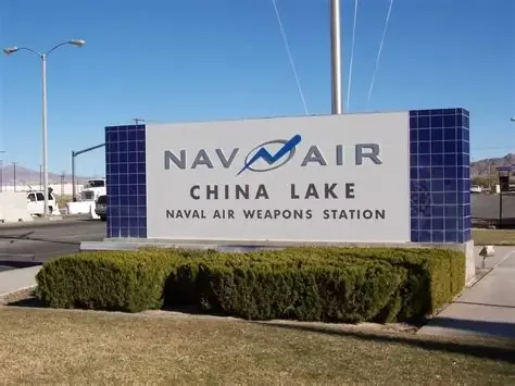 Sign for NAV AIR China Lake Naval Air Weapons Station with blue tiles and bushes in front.