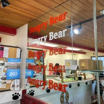 View of the interior of a bakery named 'Hungry Bear,' with red and white signage, a glass display case, and paw print decorations.