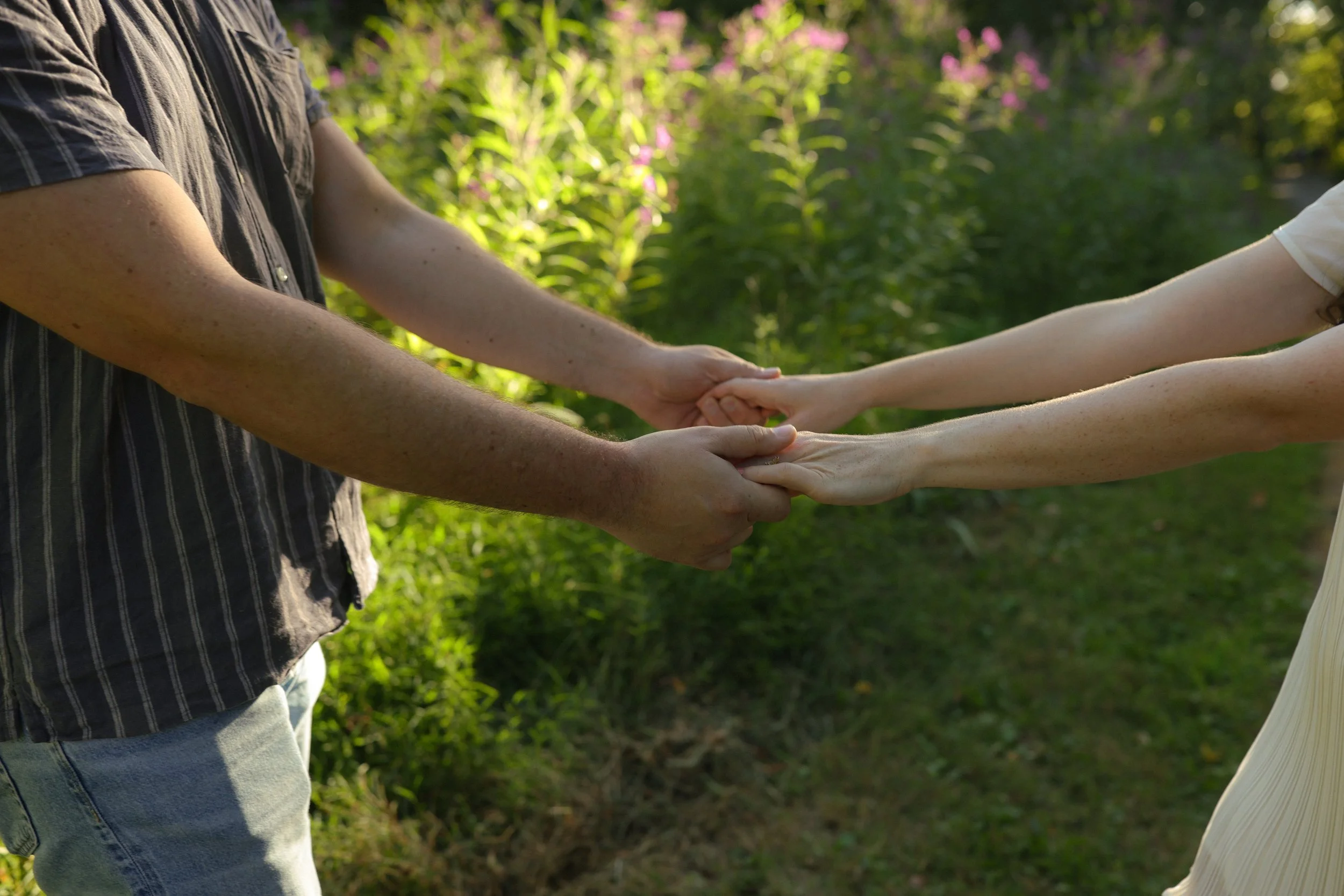 Two people holding hands outdoors in a green, natural setting.