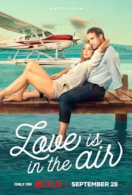 A couple relaxes on a dock near a helicopter with ocean in the background. The woman leans into the man, both appearing content. The text promotes the Netflix film 'Love is in the Air,' releasing September 28.