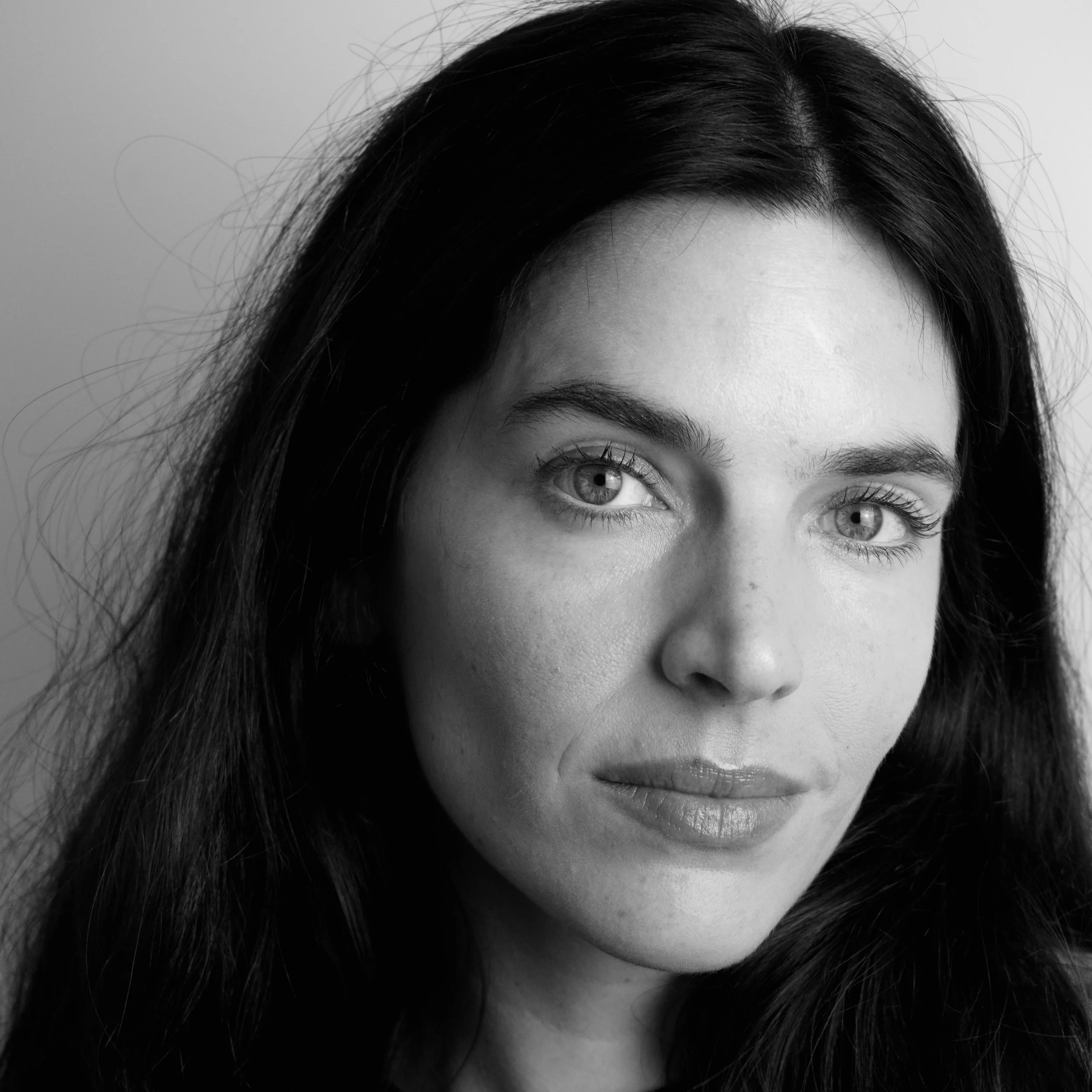 Close-up black and white portrait of a woman with dark hair and visible eye, part of her face, and some loose hair strands.
