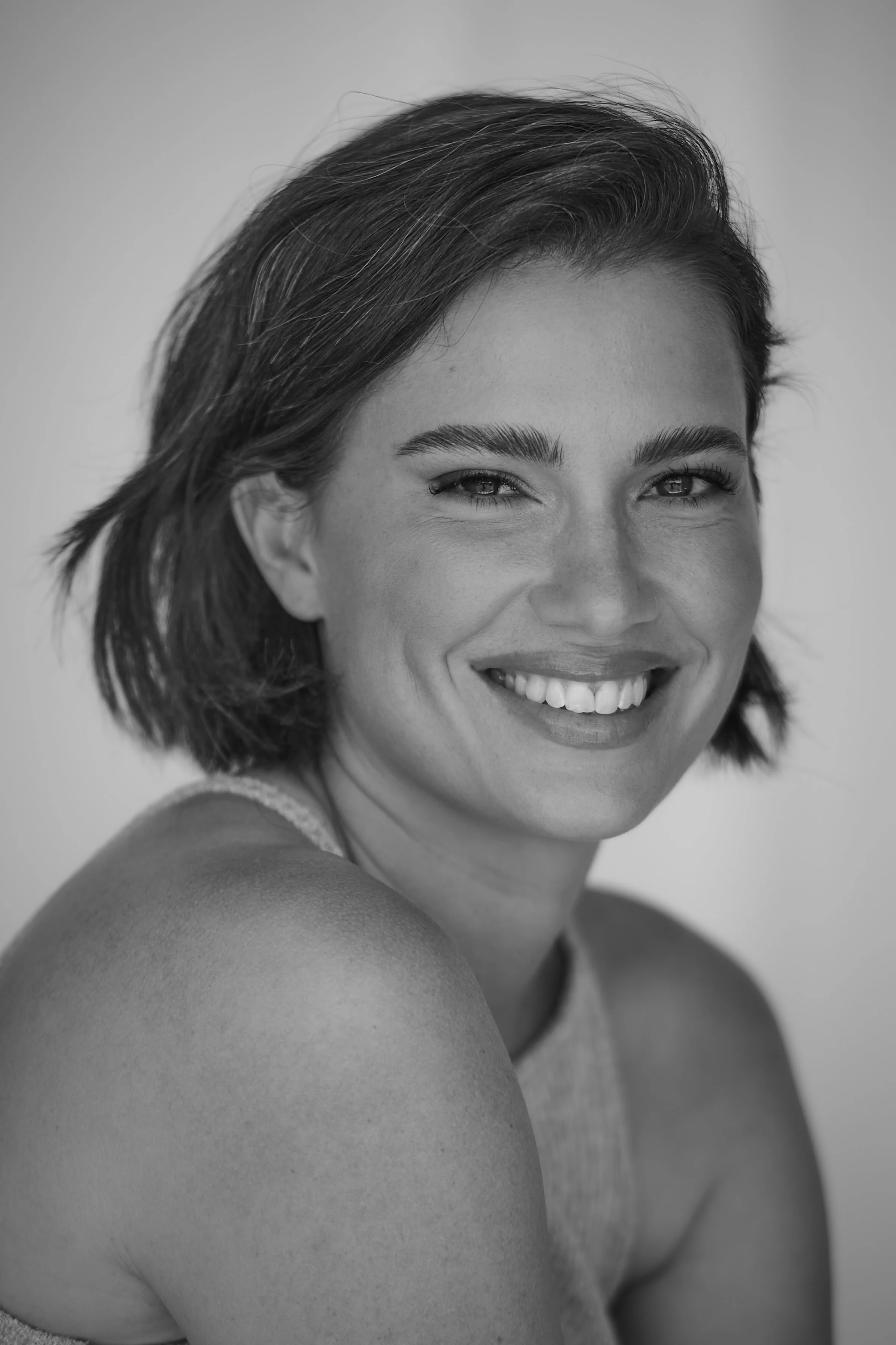 Close-up black and white photograph of a smiling woman with short dark hair, looking directly at the camera.