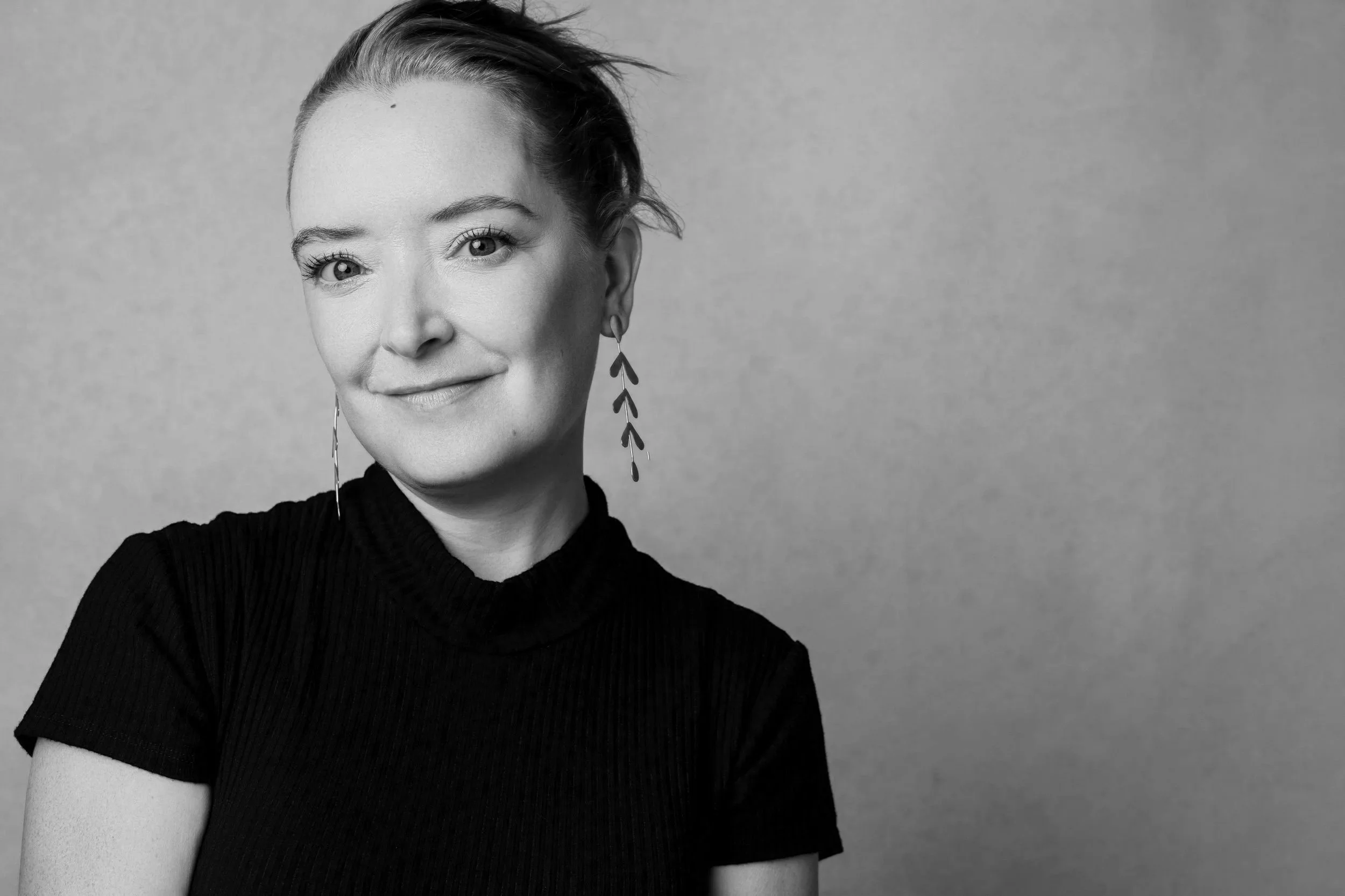 Black and white portrait of a woman with short hair, wearing a black top and long earrings, smiling gently.