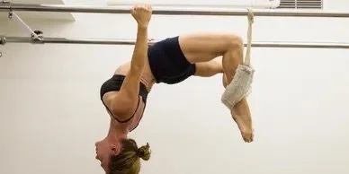 A woman performing an aerial yoga pose hanging upside down from a white metal bar