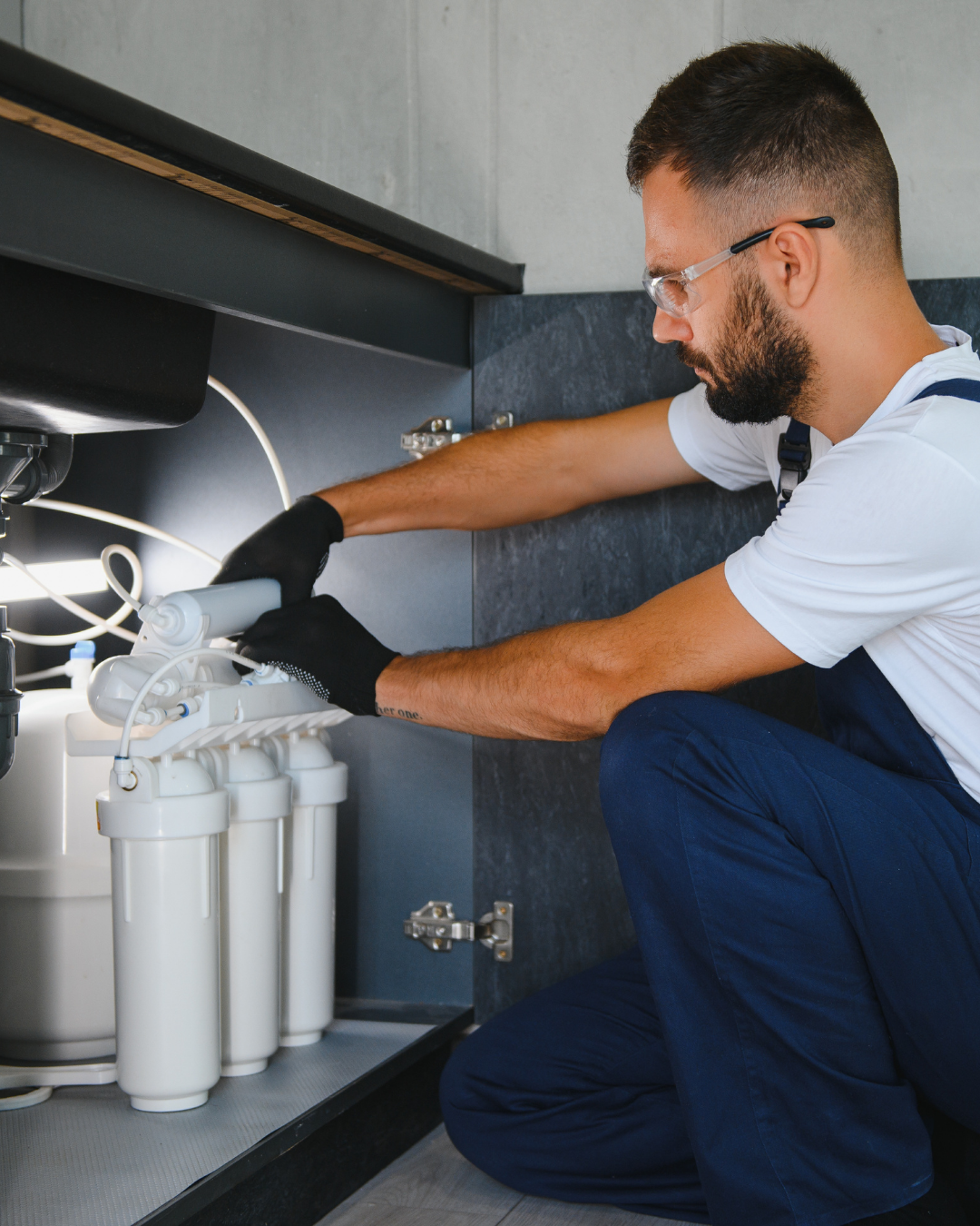 A man inspecting a water filtration system under a kitchen sink.