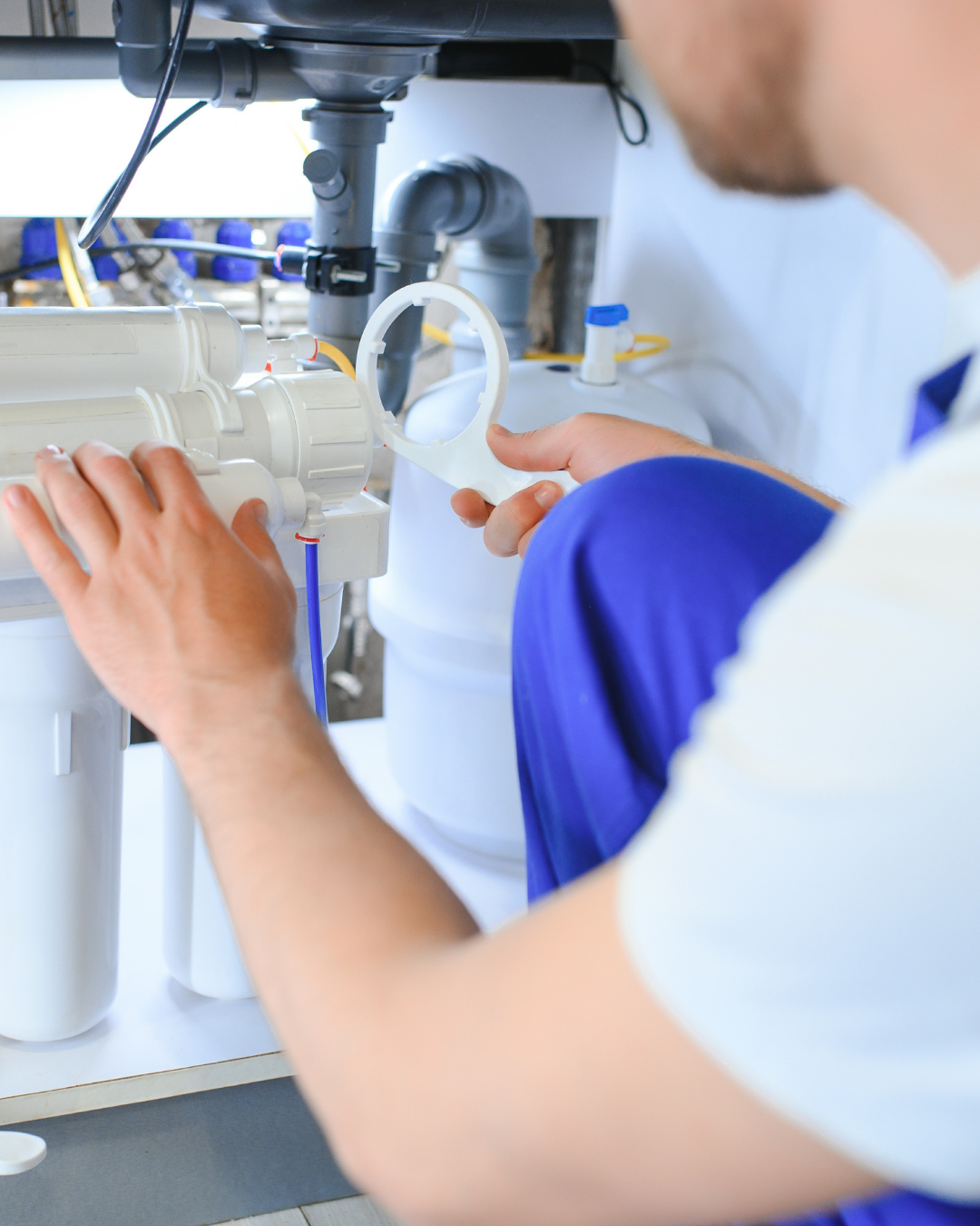 A person wearing a white and blue uniform is working with laboratory equipment, handling a circular white plastic filter or component over a water filtration system in a lab setting.