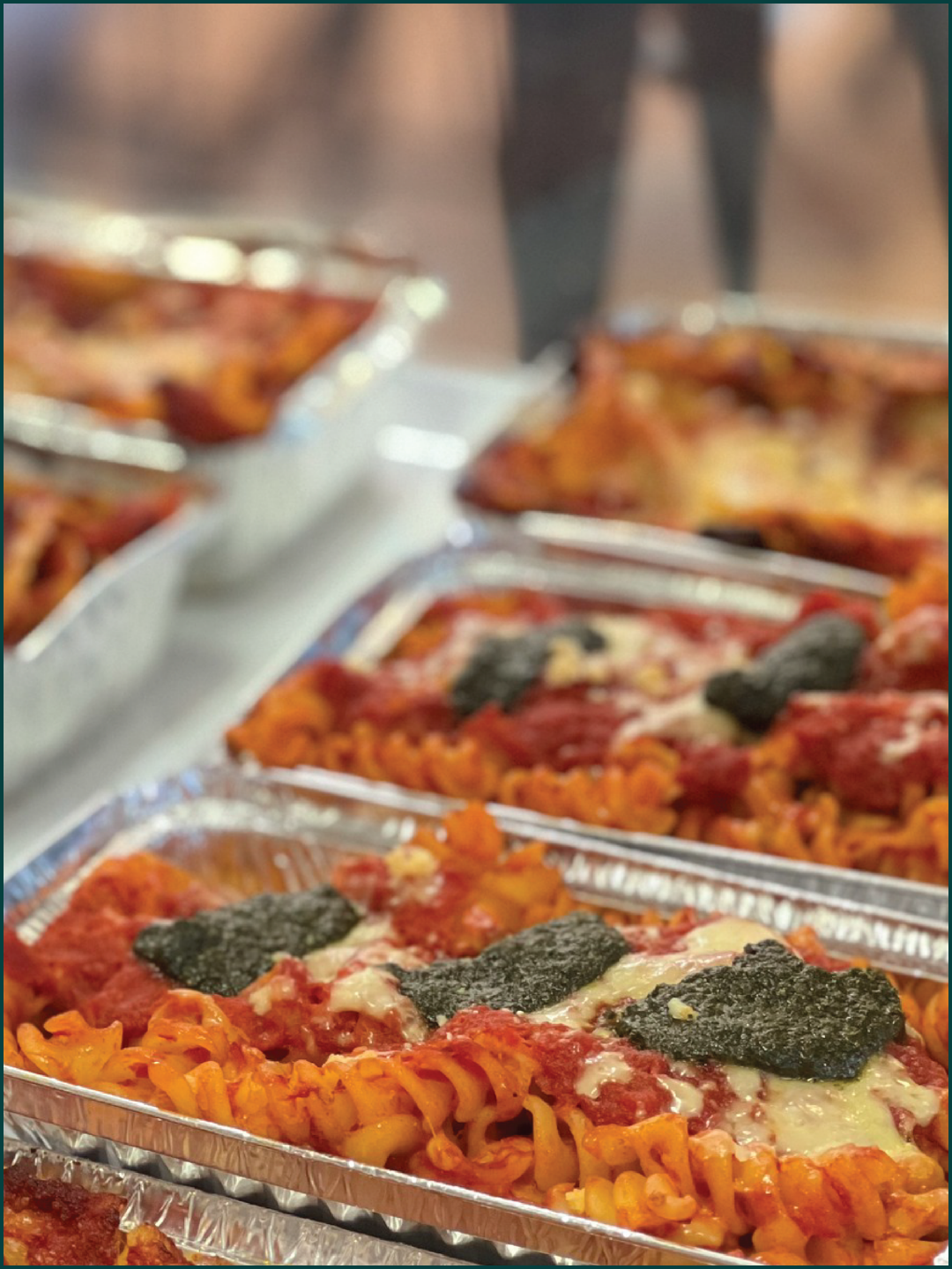 Trays of homemade baked pasta with tomato sauce, cheese, and fresh basil